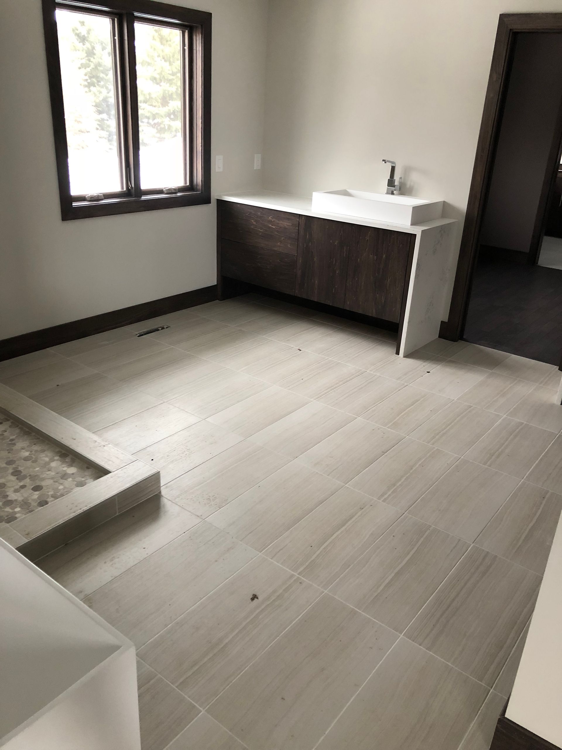 Bathroom floor tile installation | A bathroom with a sink and a window.