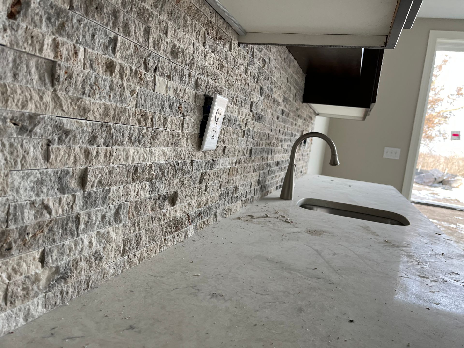 Stone backsplash | A kitchen with a sink and a brick wall behind it.