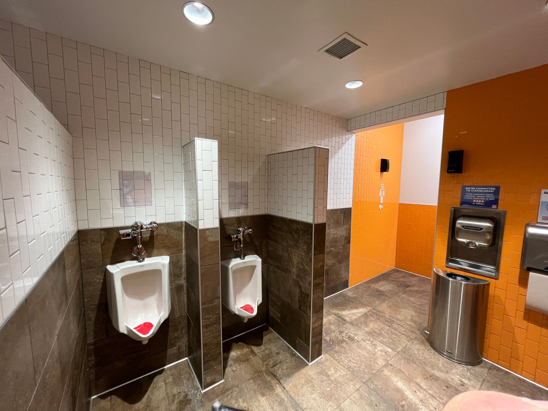 Commercial tiling contractors work | A public restroom with two urinals and a trash can.