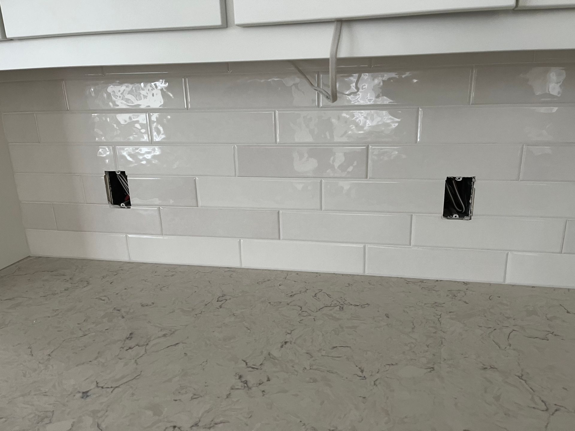 A kitchen backsplash with white tiles and a gray counter top.