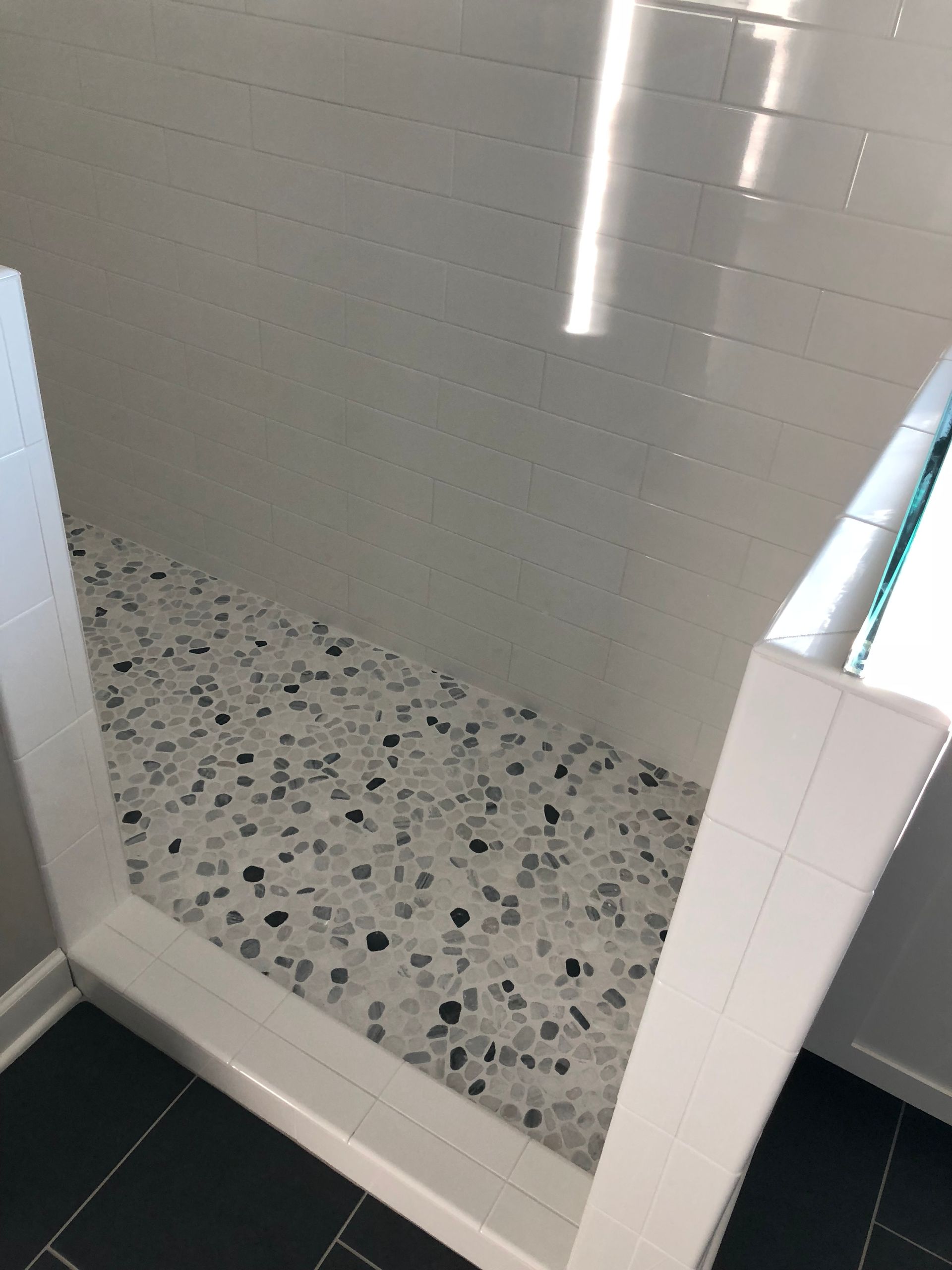 A bathroom with a walk in shower with black and white tiles.