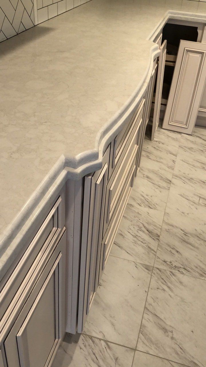 A kitchen with white cabinets and marble floors.