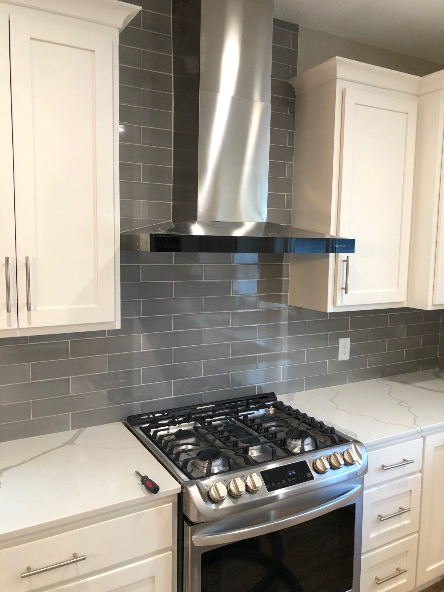 A kitchen backsplash with white cabinets , a stove , and a hood.