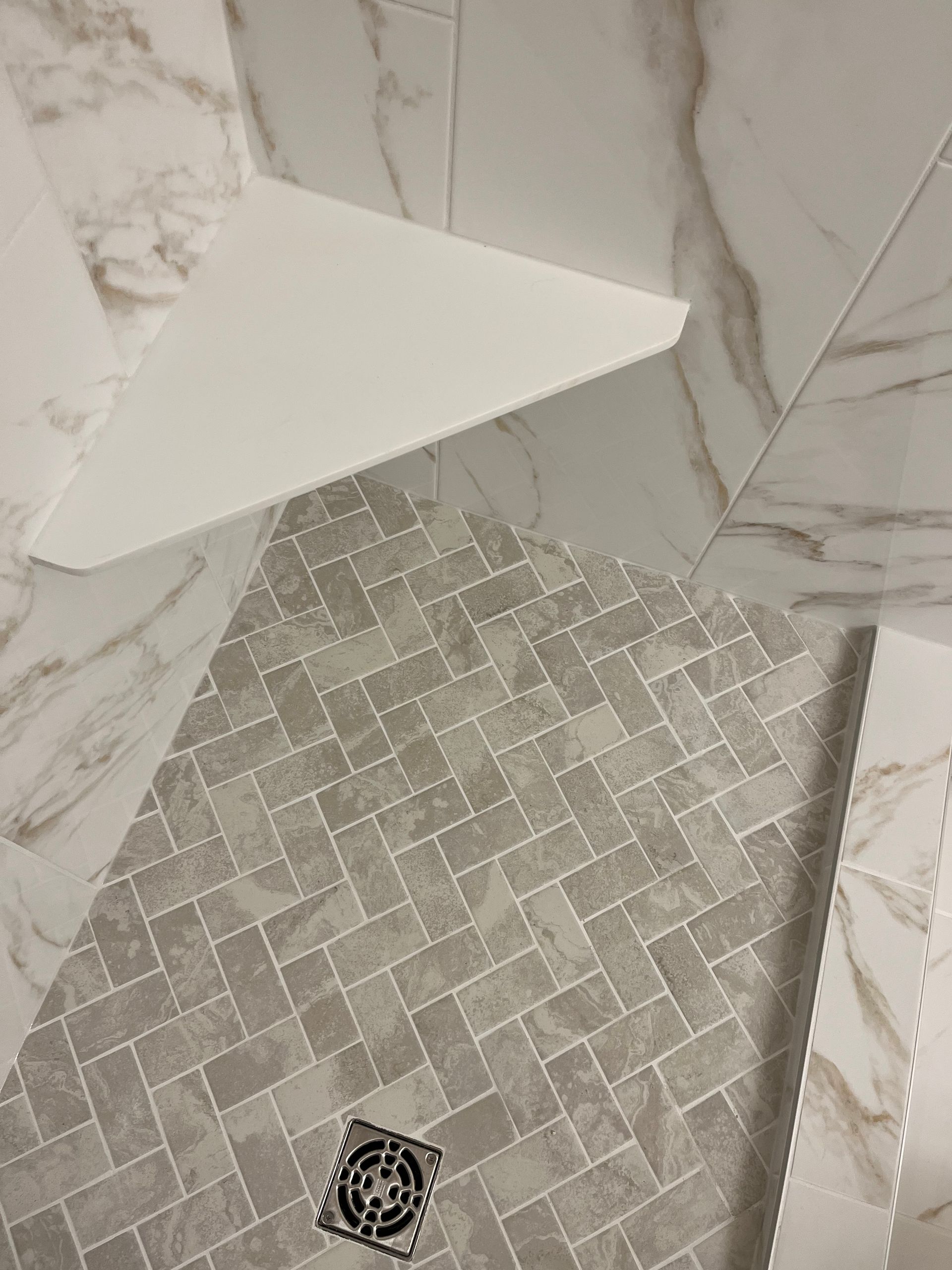 A shower with a drain on the floor and a marble wall.