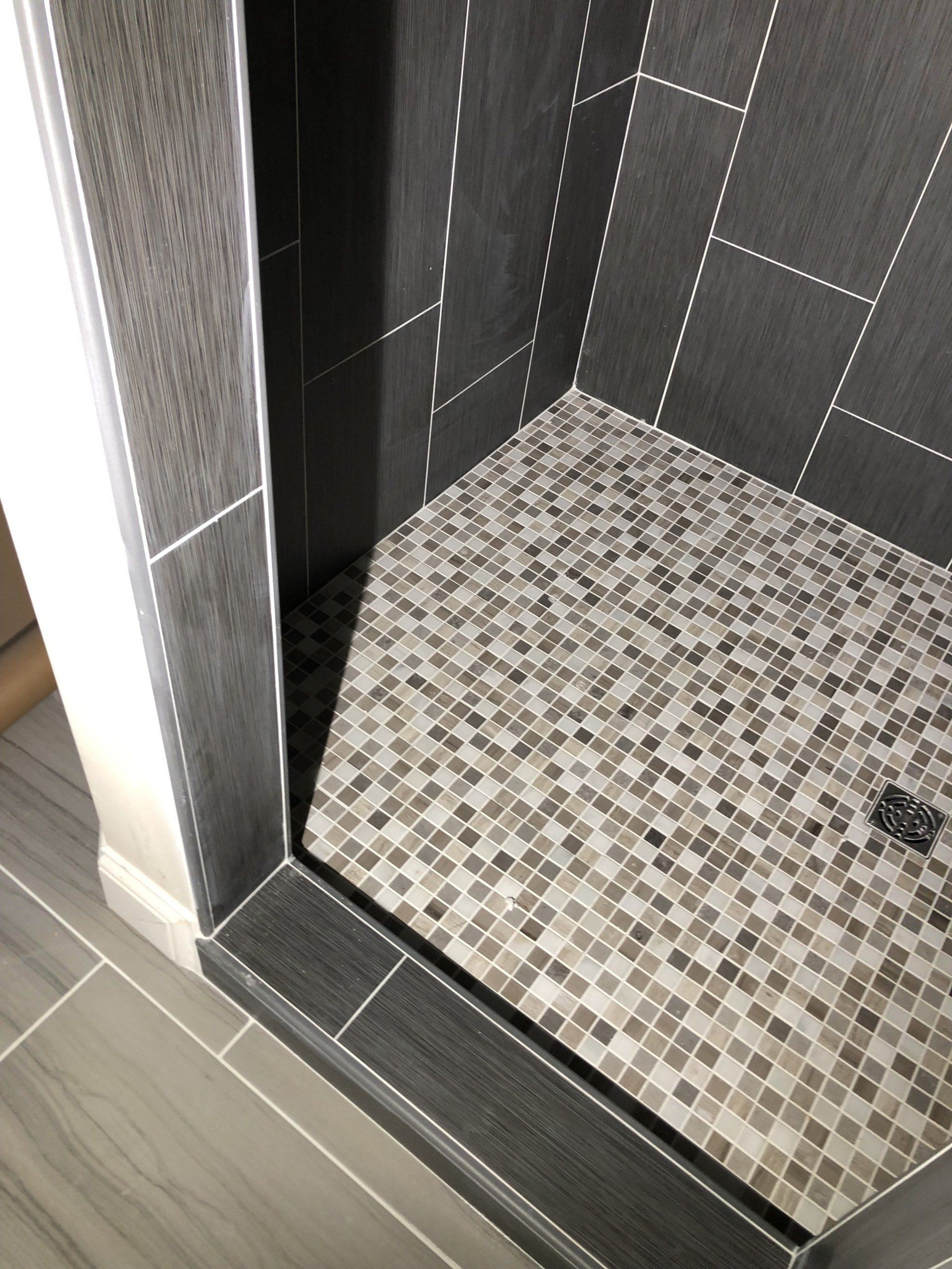 Custom shower tile designs | A shower stall with a mosaic tile floor in a bathroom.
