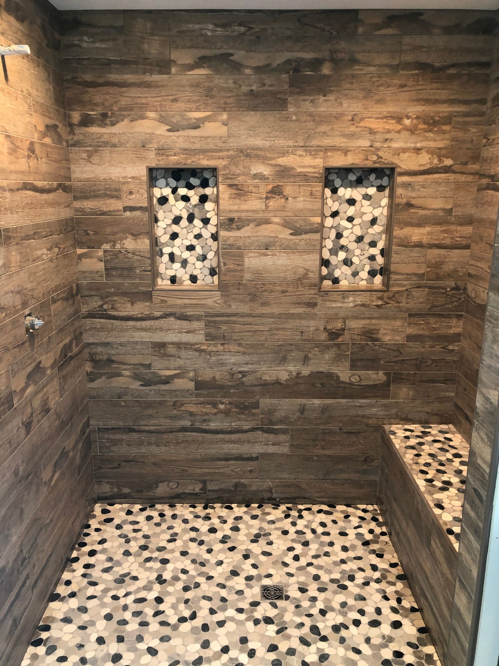 Shower remodeling | A shower with a wooden wall and a mosaic floor.