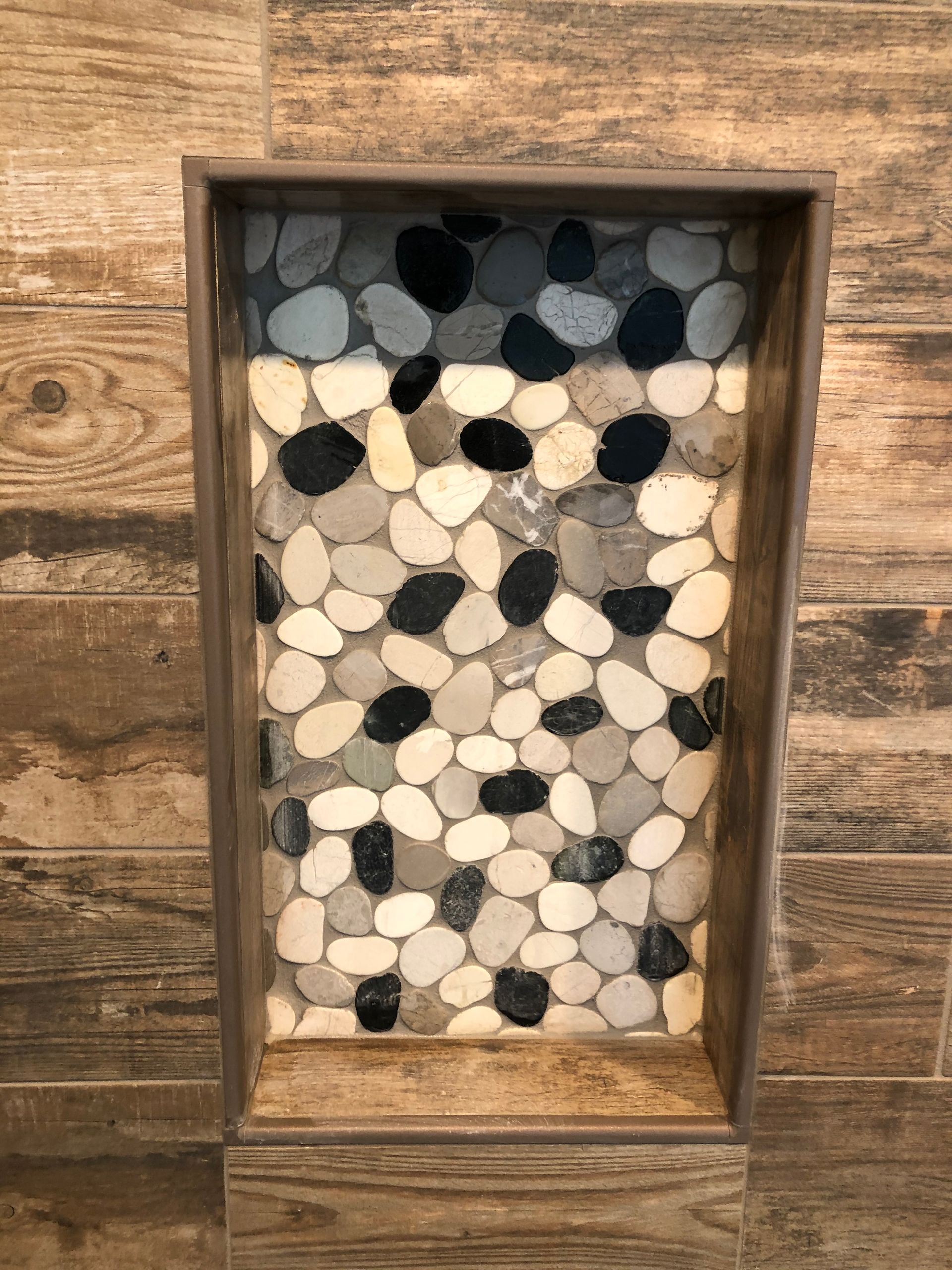 A shower niche with a mosaic of rocks on a wooden wall.