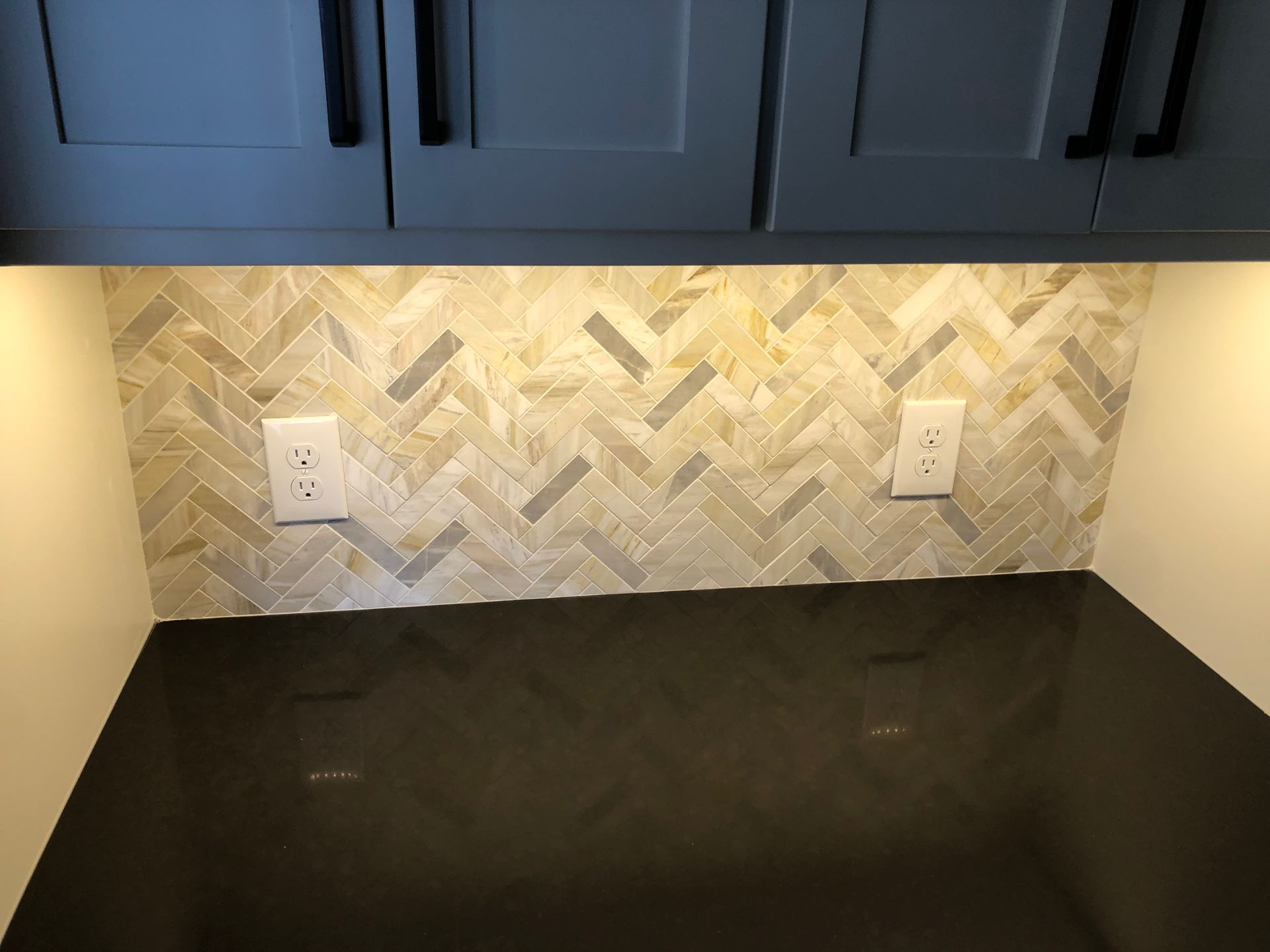 A kitchen with a black counter top and a herringbone tile wall.