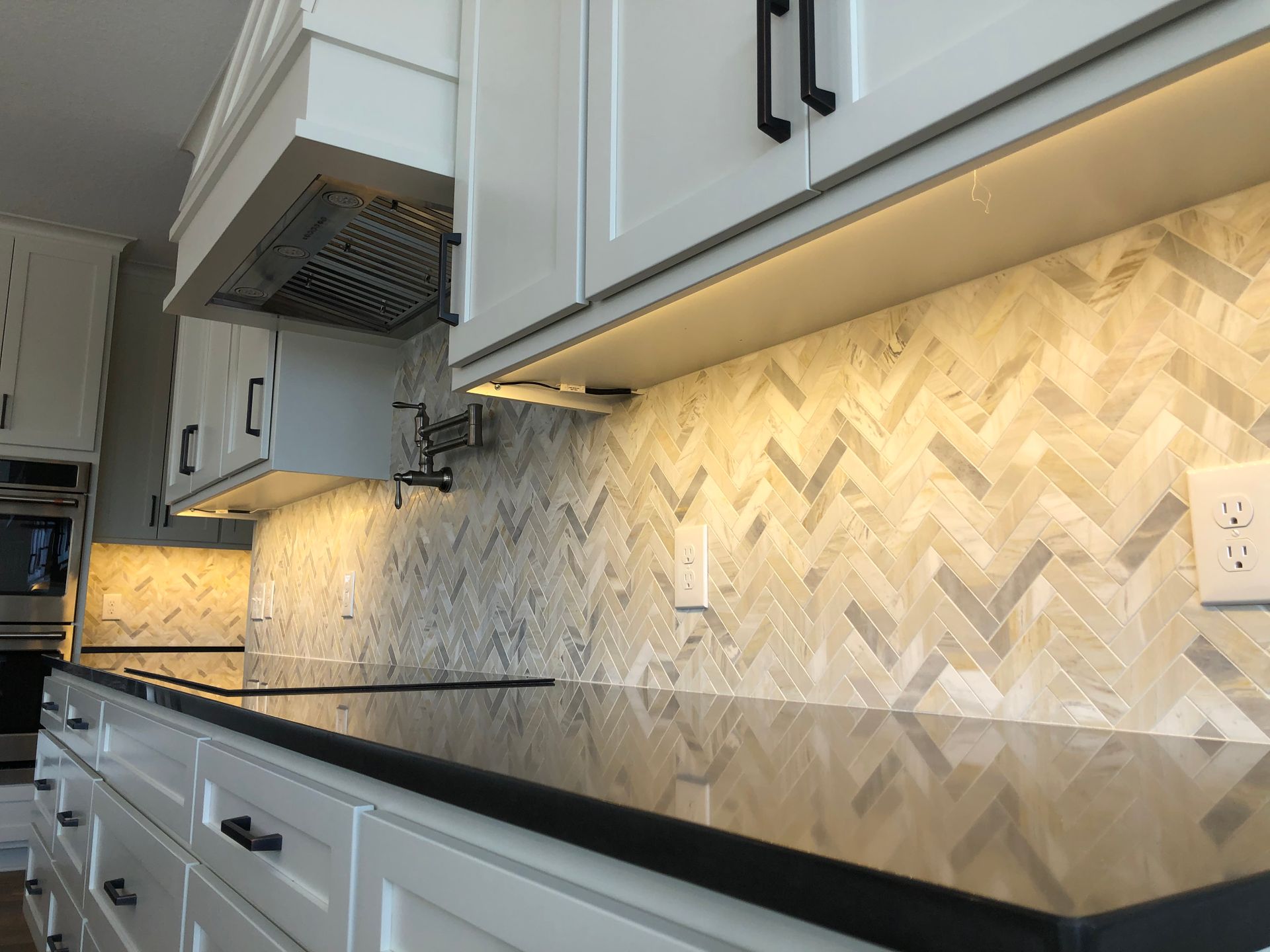 A kitchen with white cabinets and black counter tops and a herringbone tile backsplash.