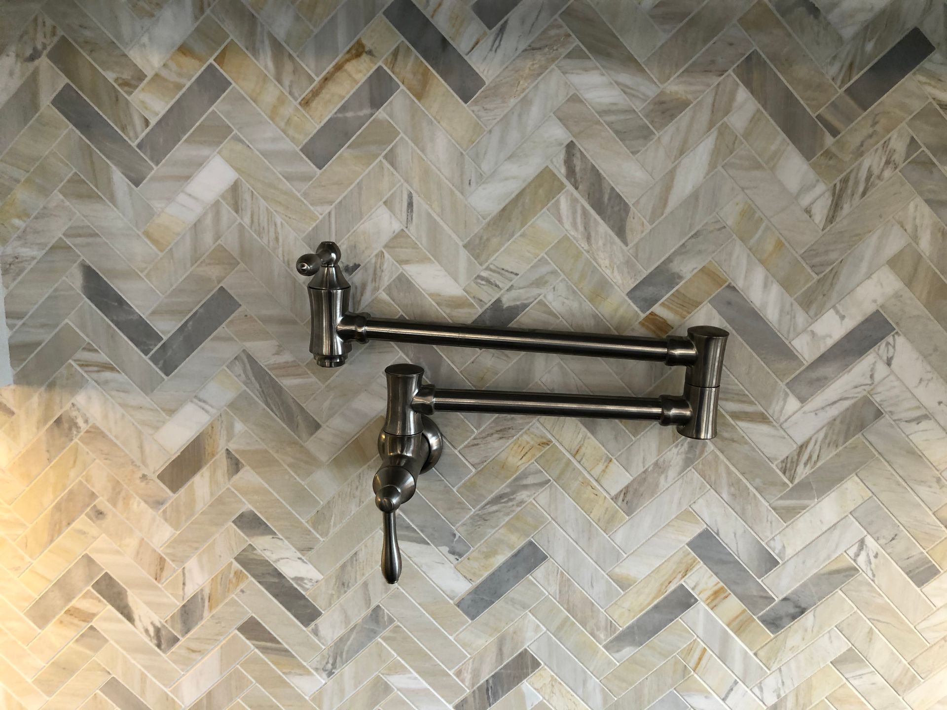 A pair of pot filler faucets hanging on a herringbone tile wall.