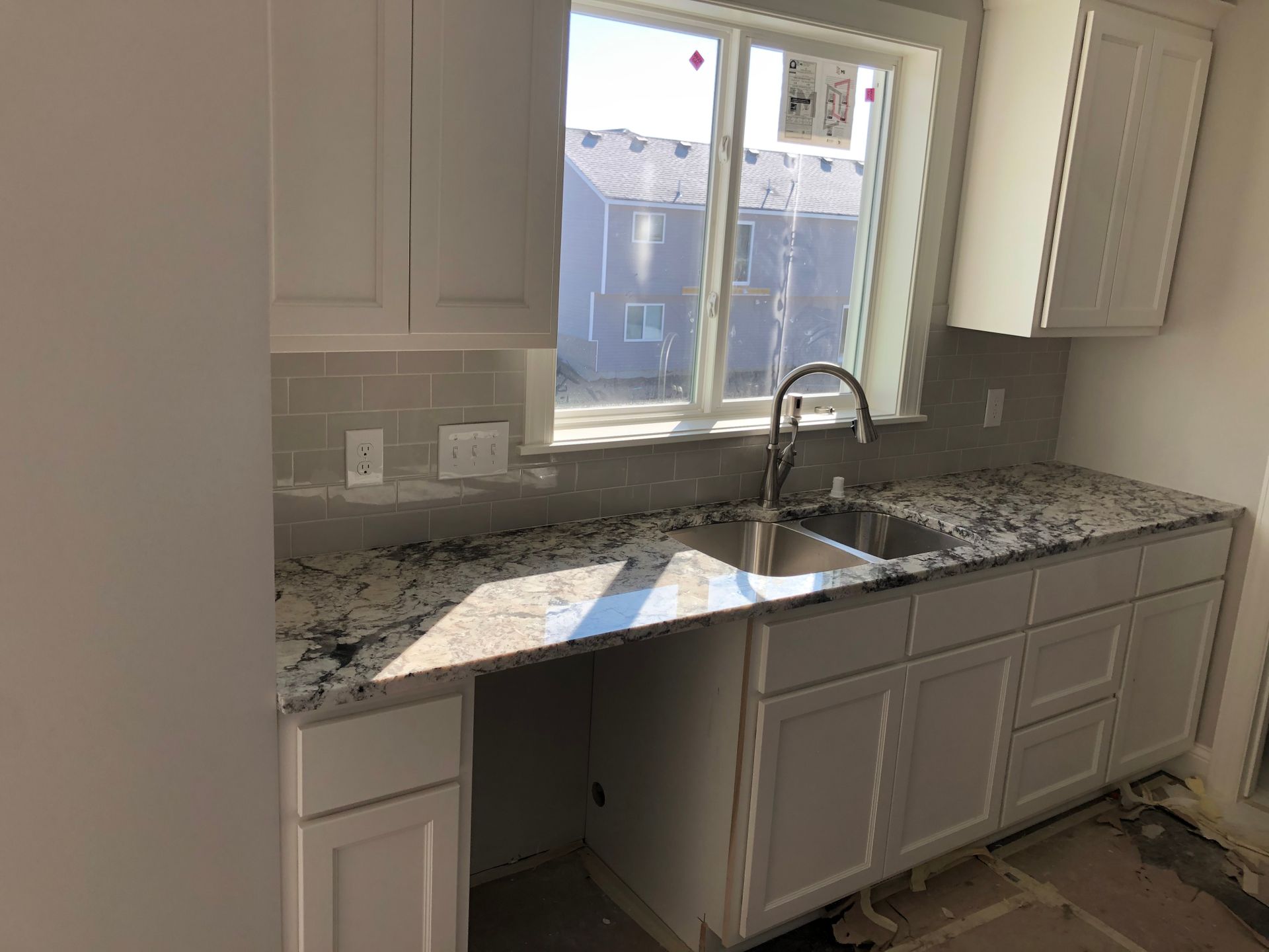 A kitchen with white cabinets , granite counter tops , a sink and a window.