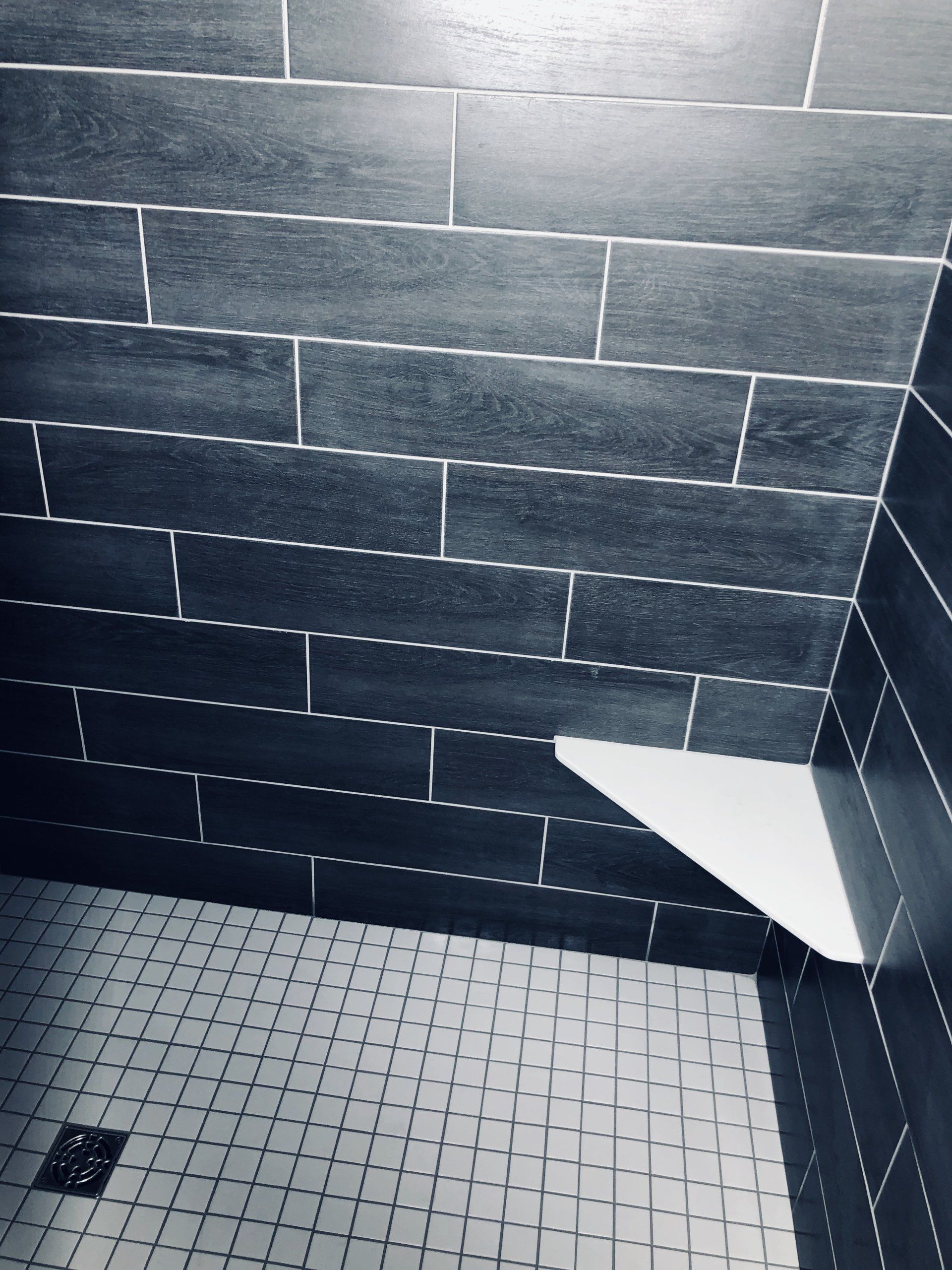 A tile shower with black tiles and a white shelf