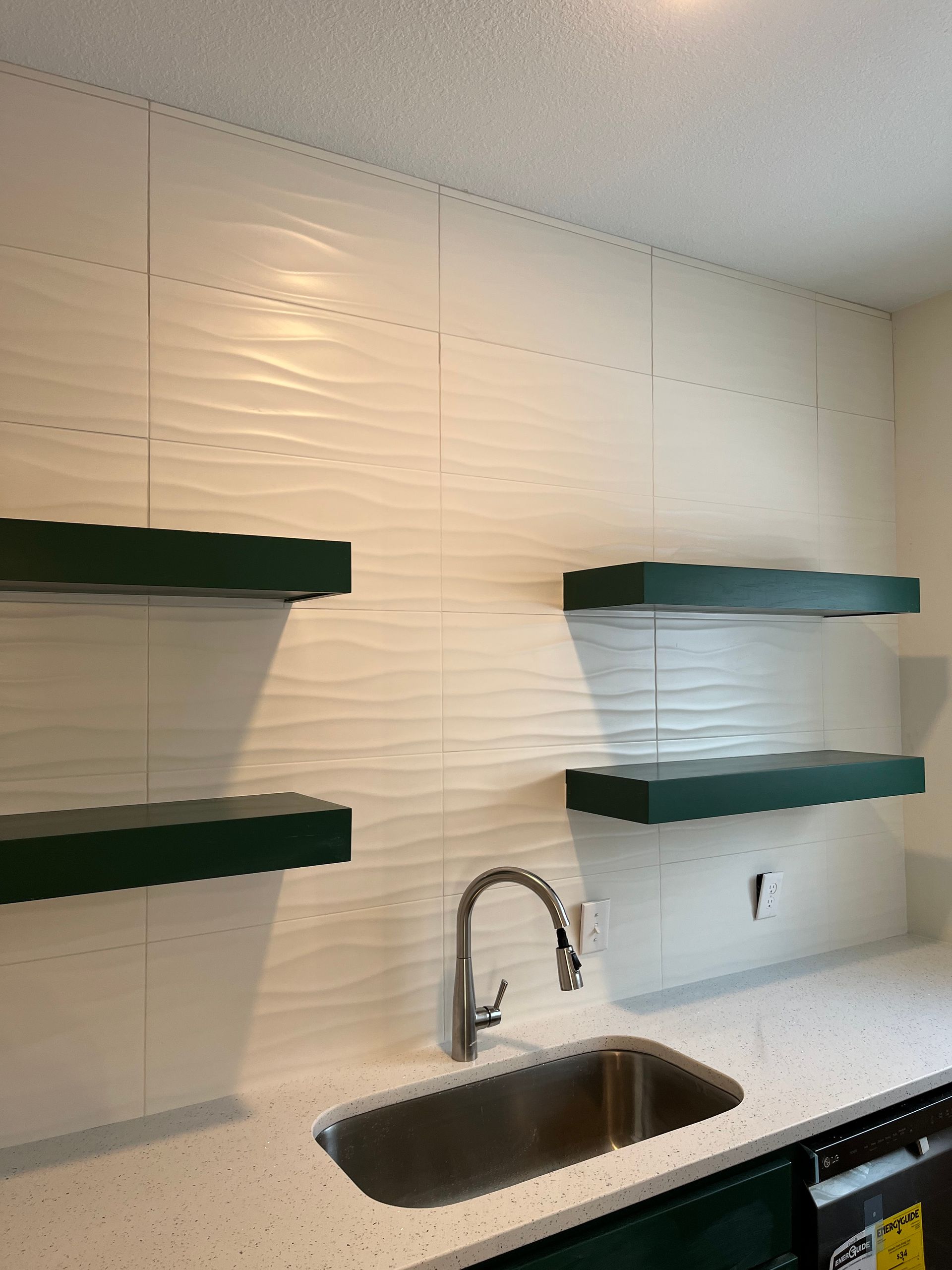 A kitchen tile wall with a sink and green shelves on the wall