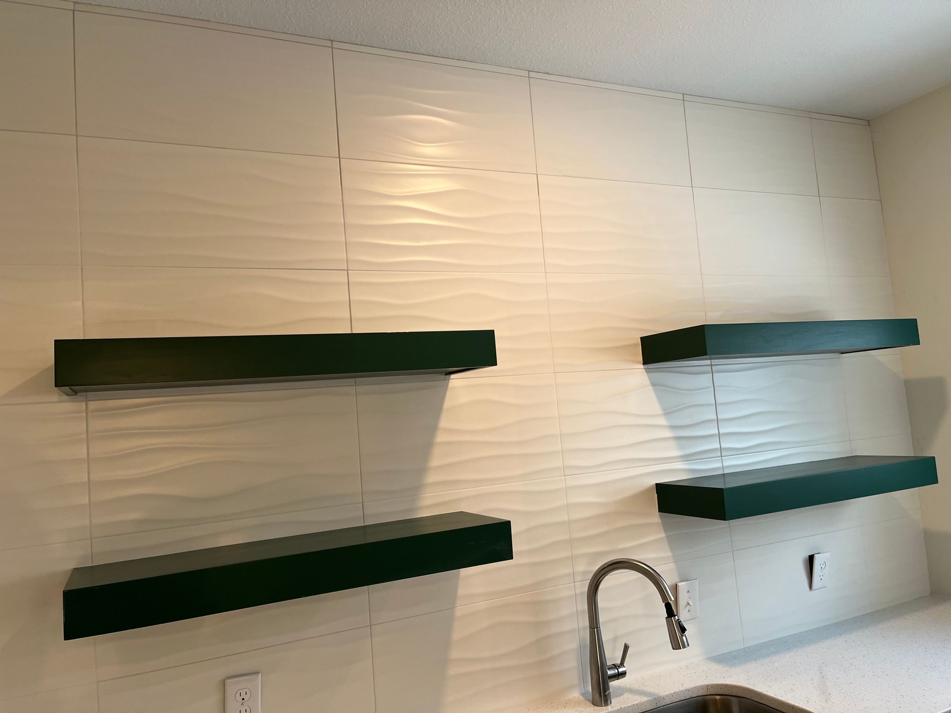 A kitchen tile wall with two green shelves and a sink