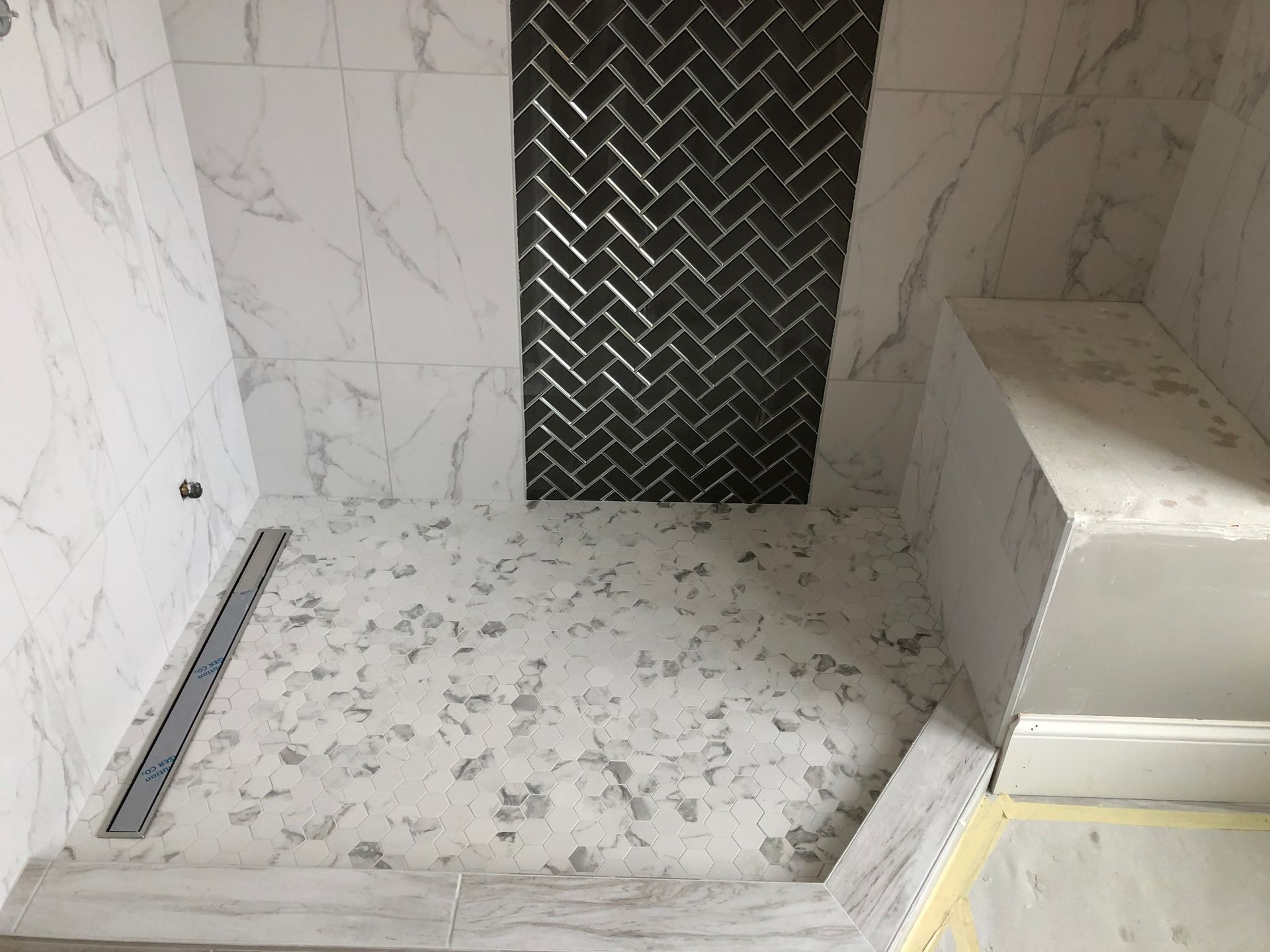 A bathroom with a walk in shower and a herringbone tile wall.