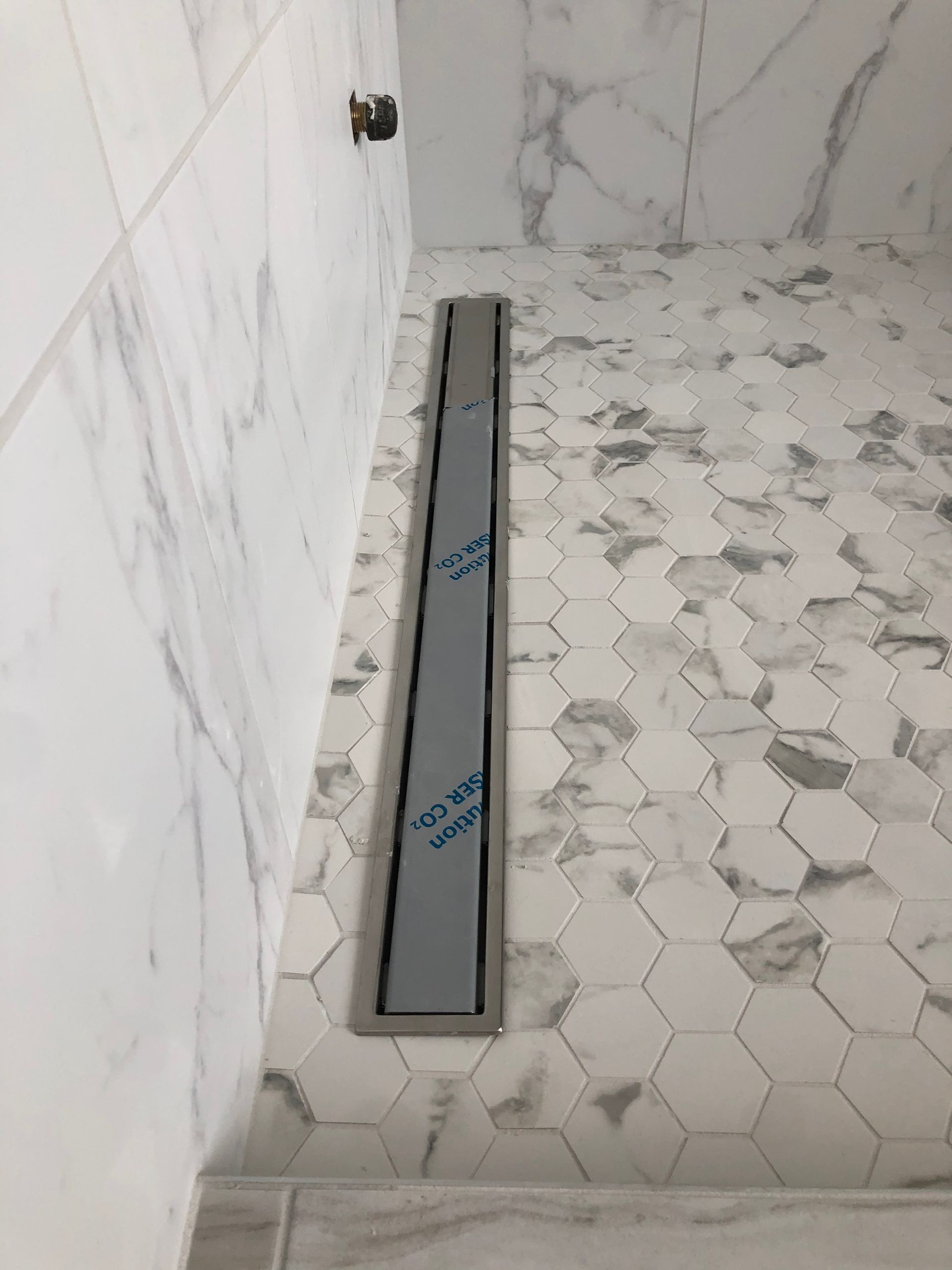 A shower with a drain on the floor and marble tiles.