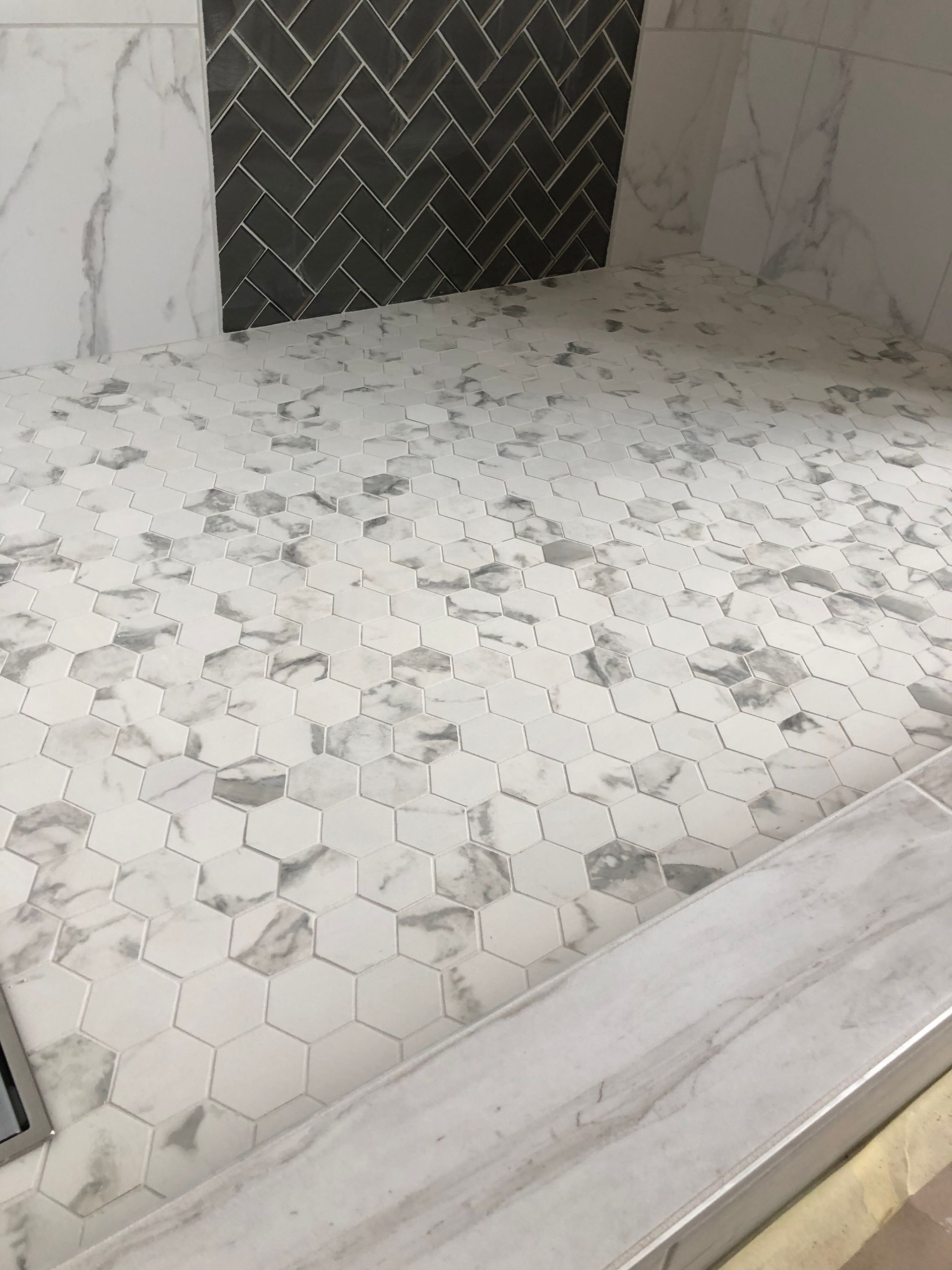 A shower stall with a marble tile floor and a herringbone pattern on the wall.