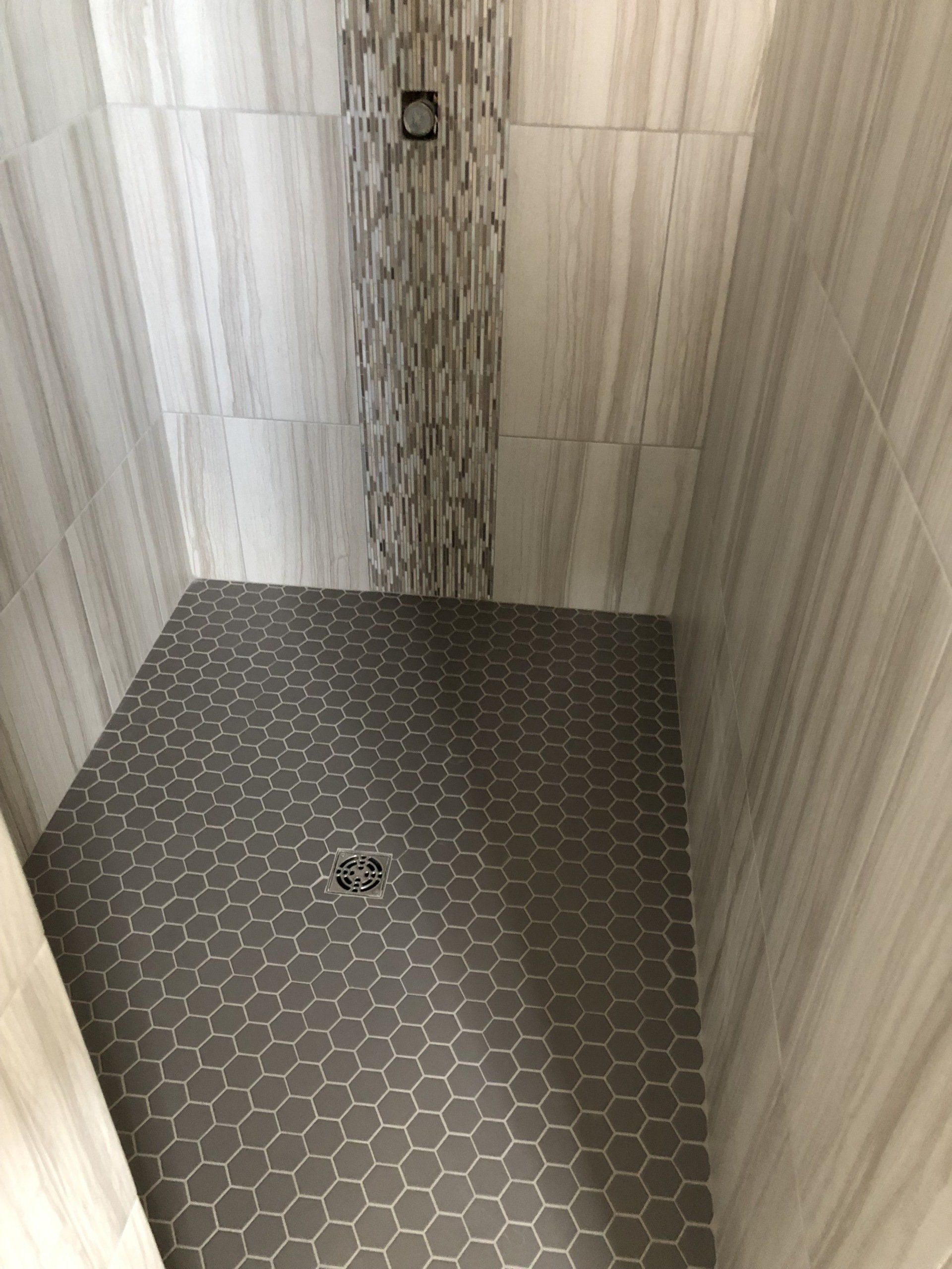 Elderly shower remodel | A walk in shower with hexagonal tiles on the floor and walls.