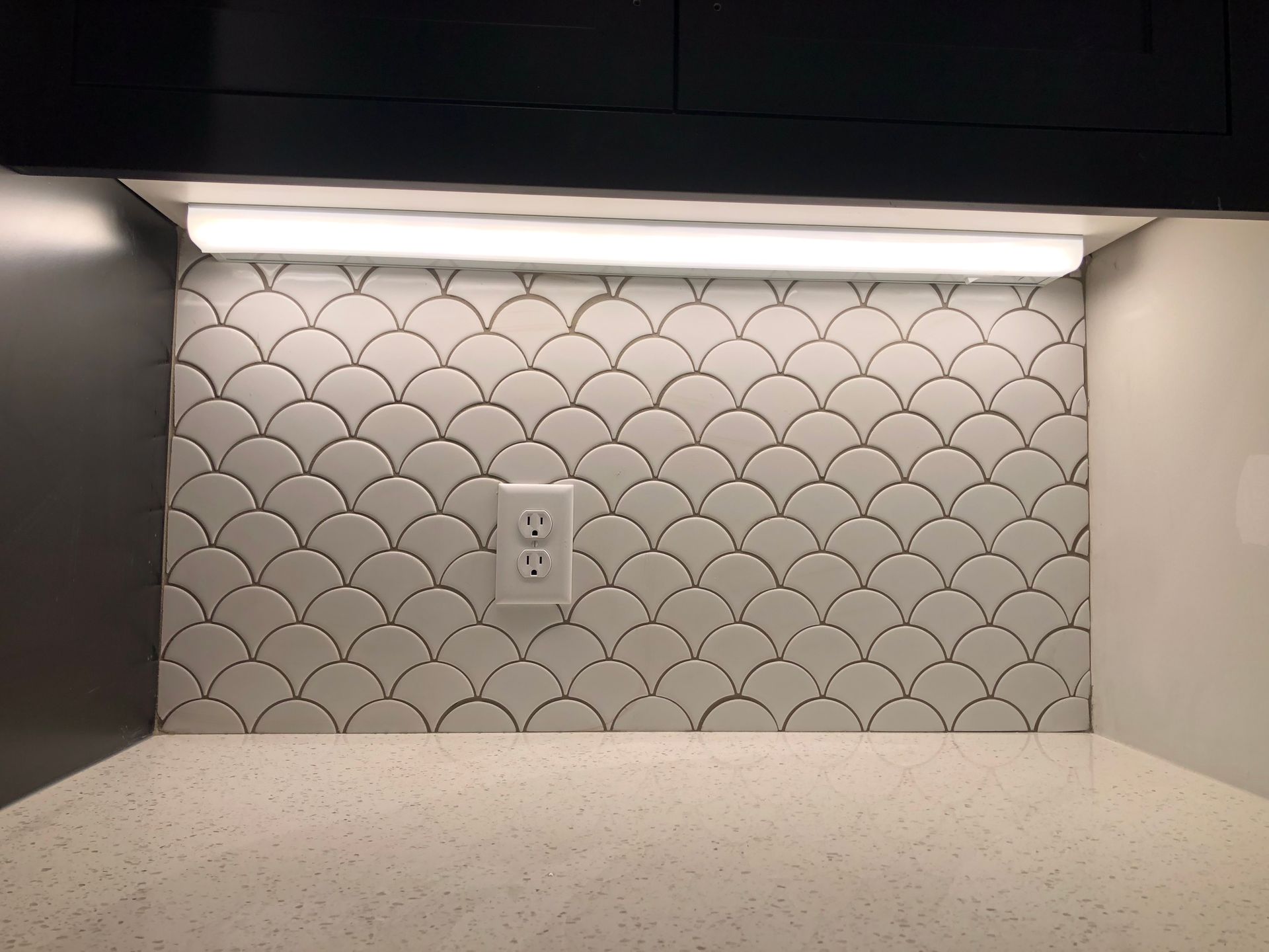 A white tile backsplash with a fish scale pattern