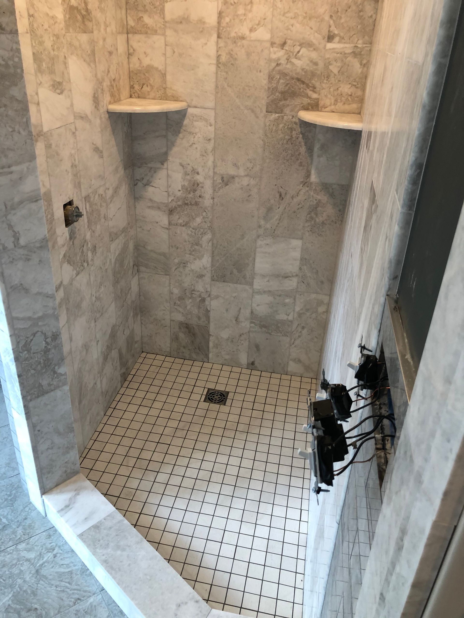 A shower stall with a tiled floor and shelves in a bathroom.