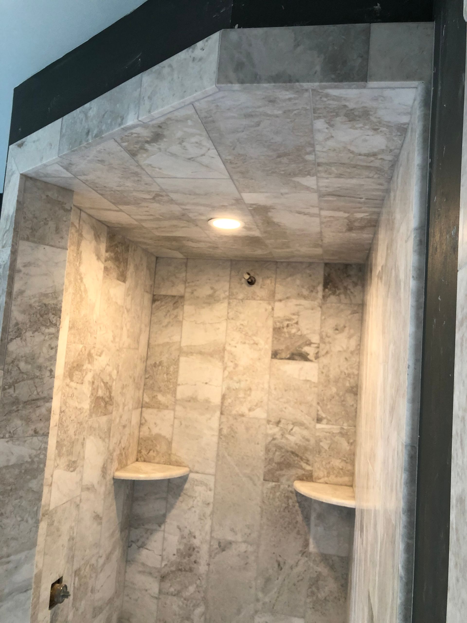 A bathroom with tiled walls and shelves and a ceiling.