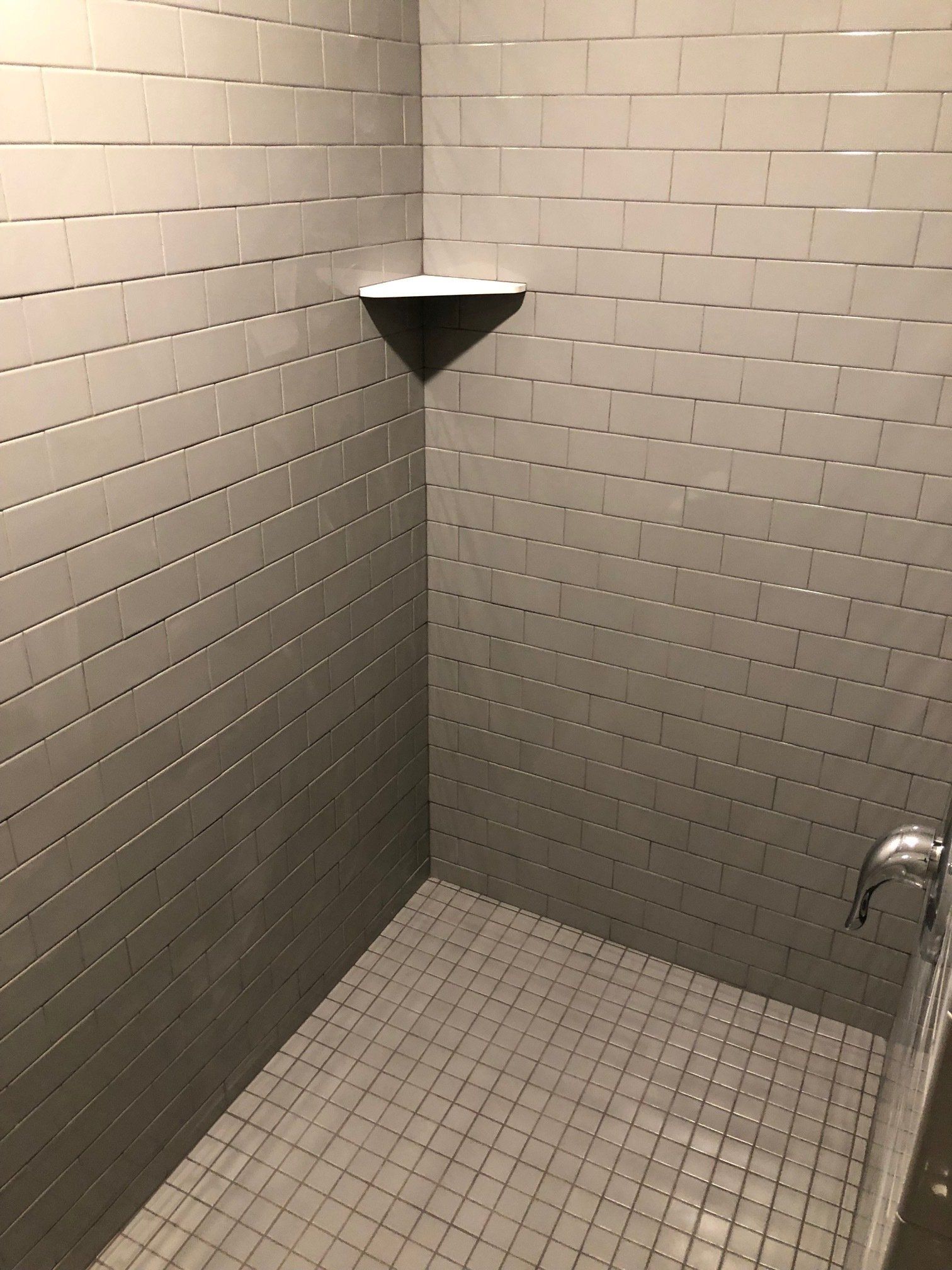 A shower with a tiled floor and a shelf in the corner.