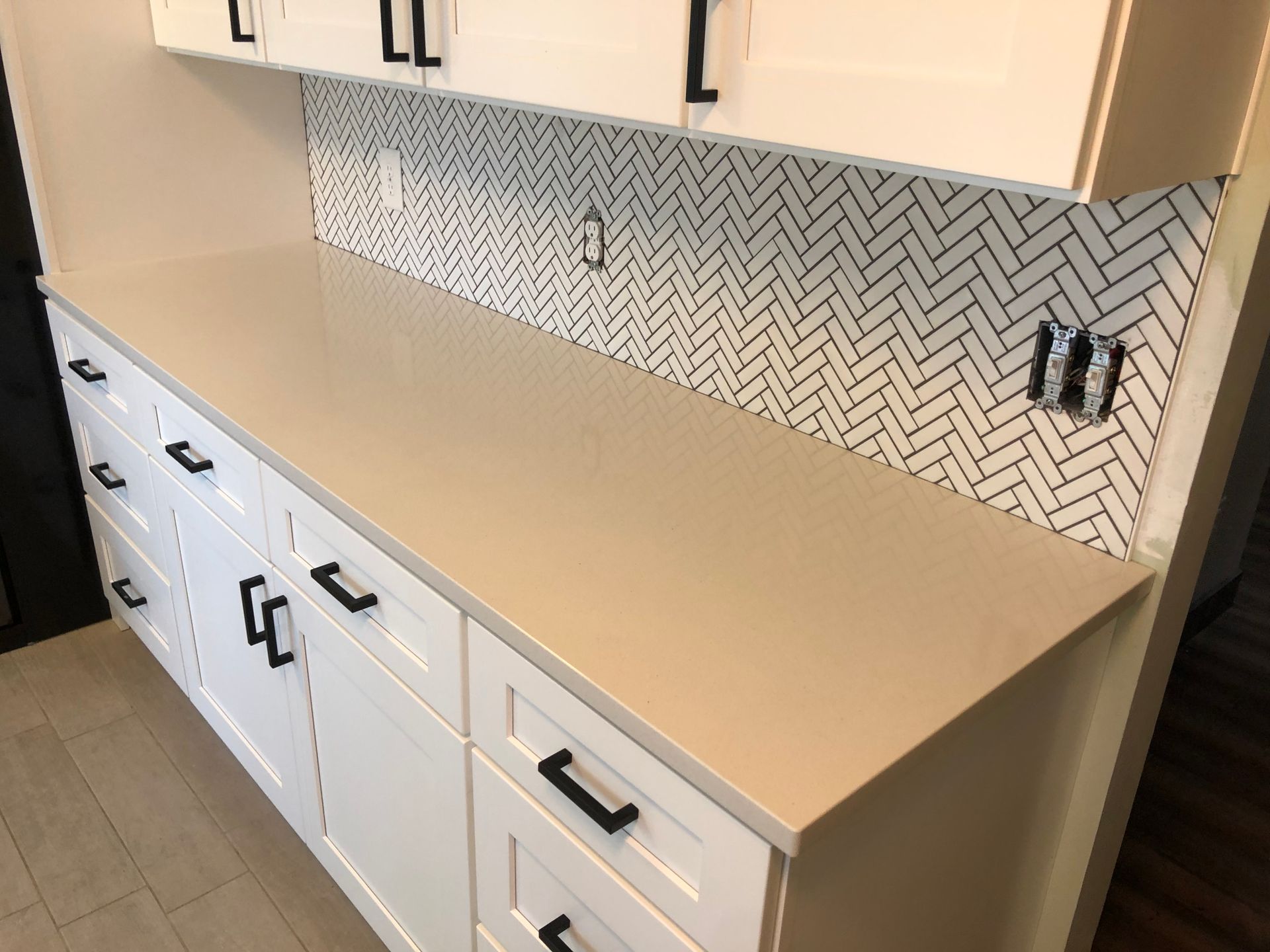 Kitchen backsplash, a counter with white cabinets and black handles.