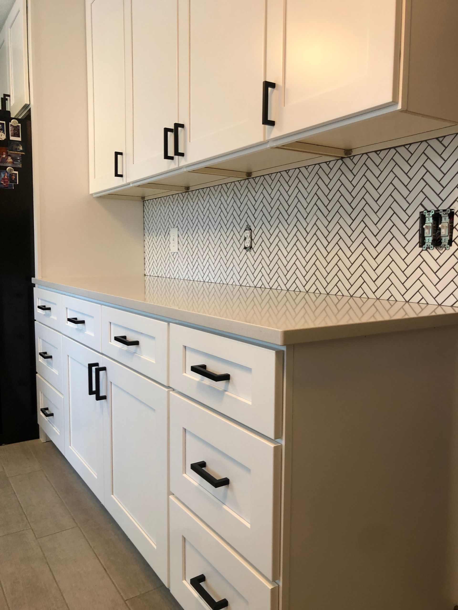 New backsplash installed | A kitchen with white cabinets and black drawers and a black refrigerator.