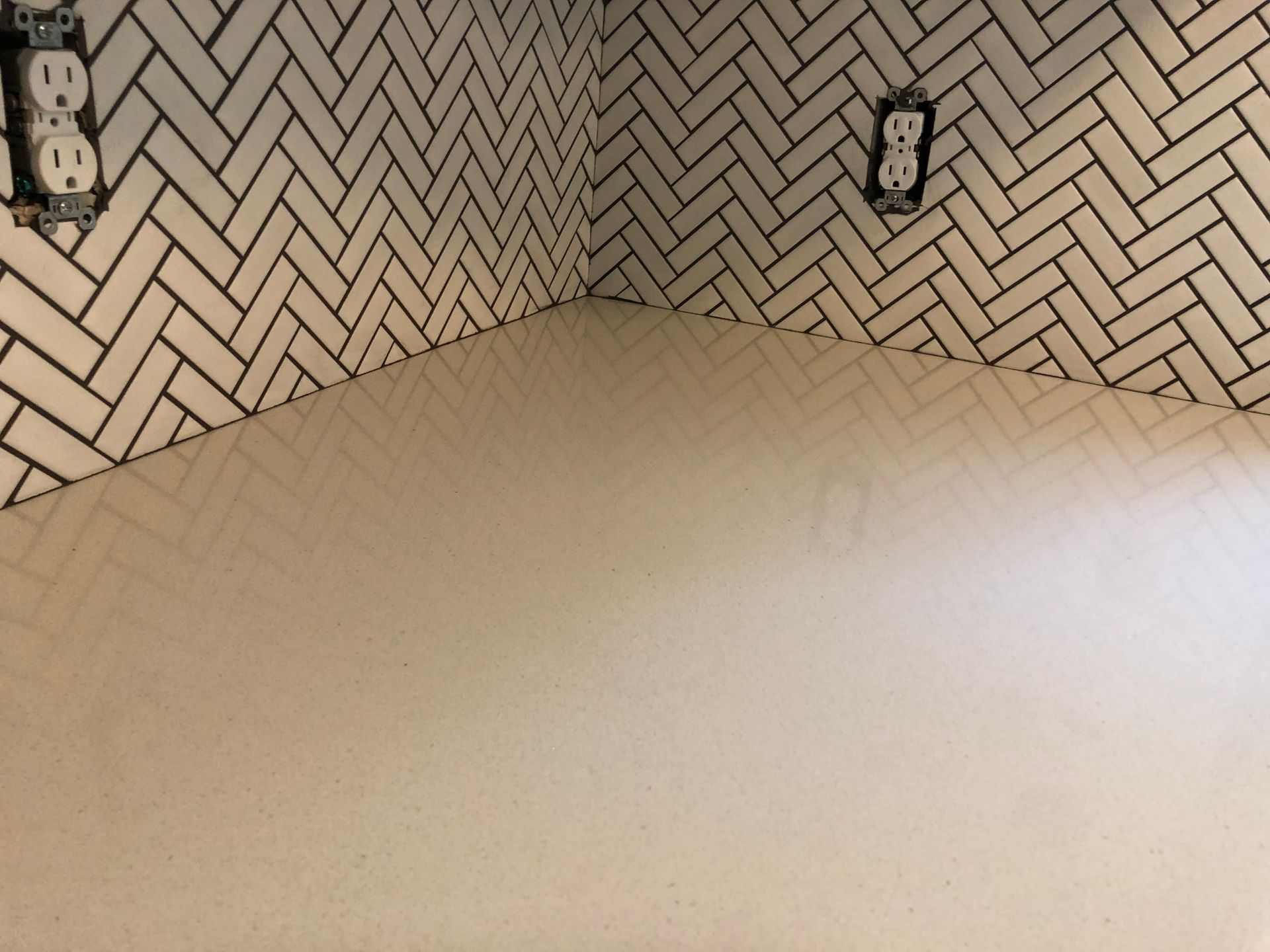 A corner of a room with a herringbone pattern on the backsplash