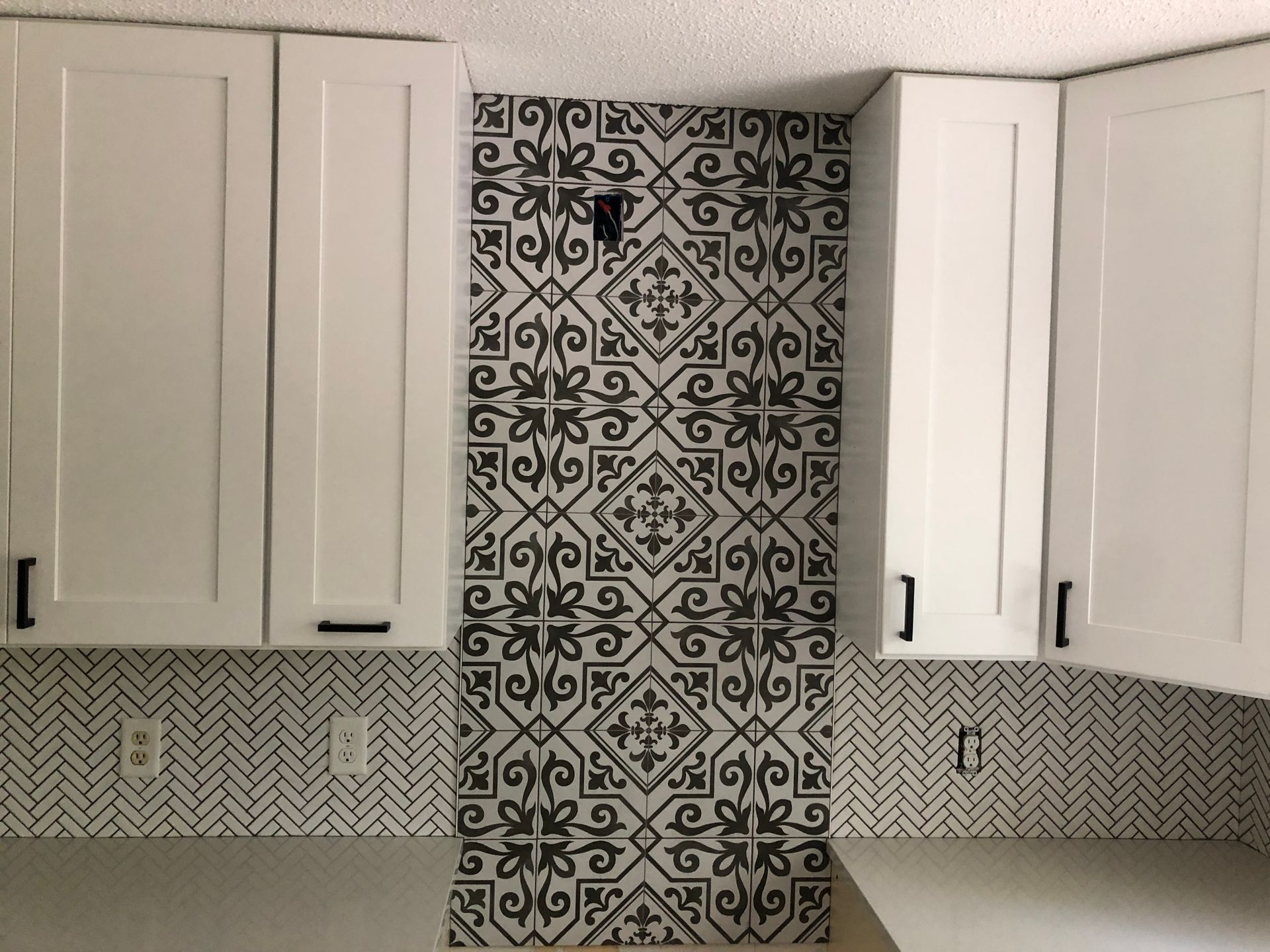 A kitchen with white cabinets and black tiles on the wall