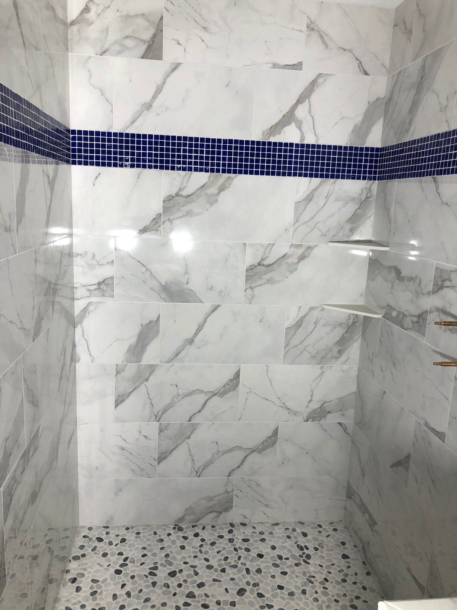 A shower with marble tiles and a blue mosaic border.