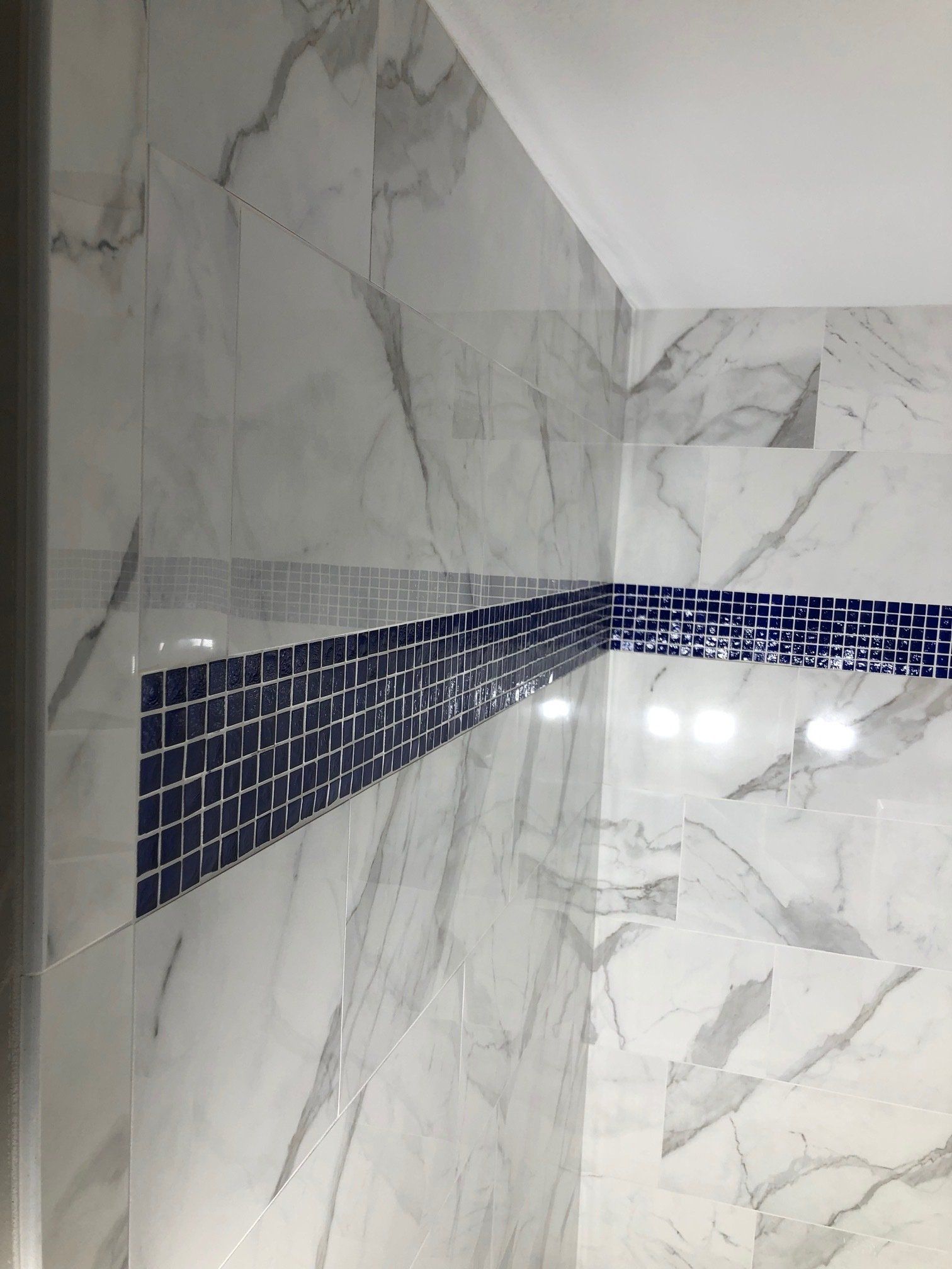 A bathroom with marble tiles and a blue mosaic border.
