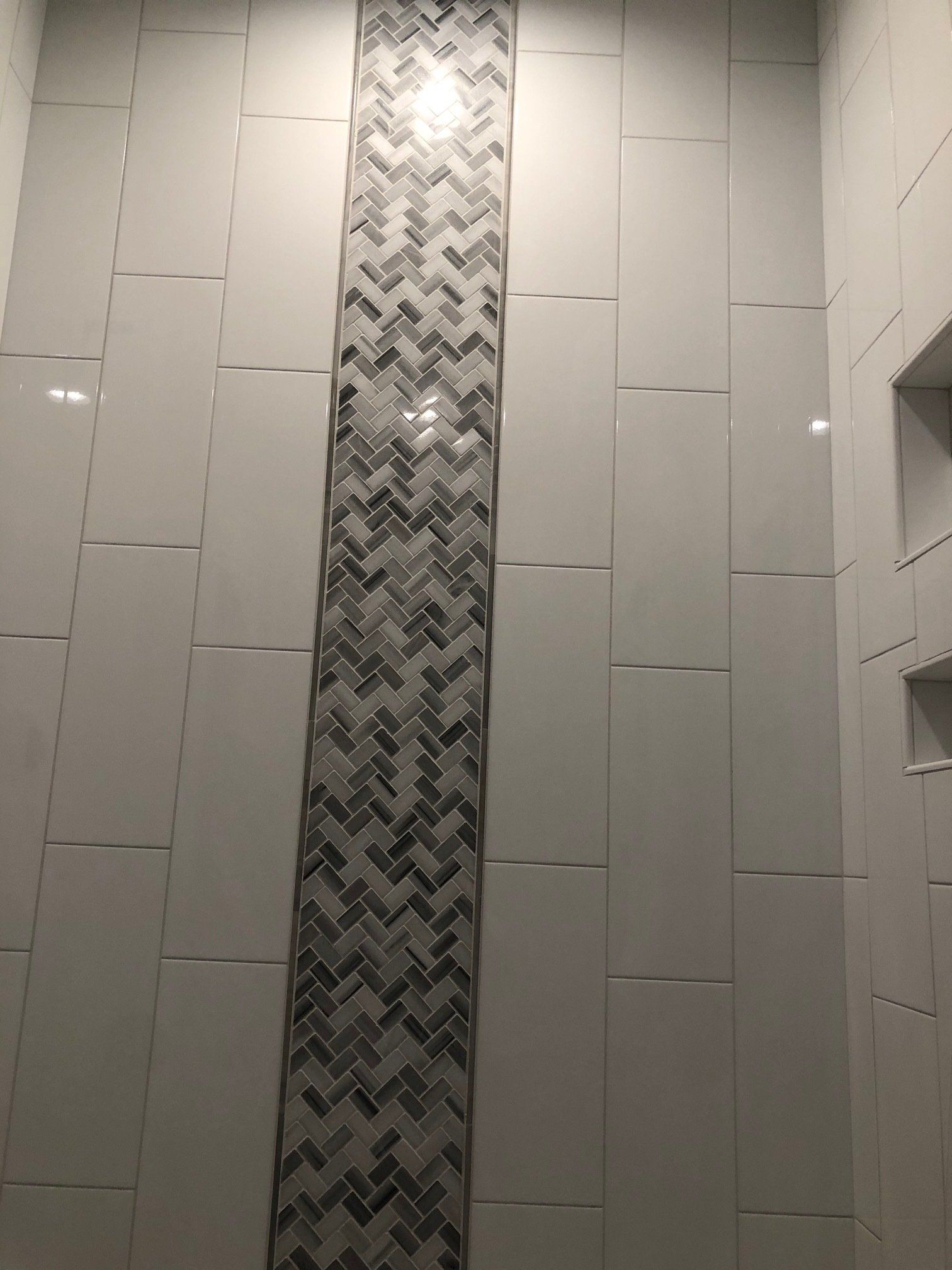 A shower with white tiles and a herringbone pattern on the wall.