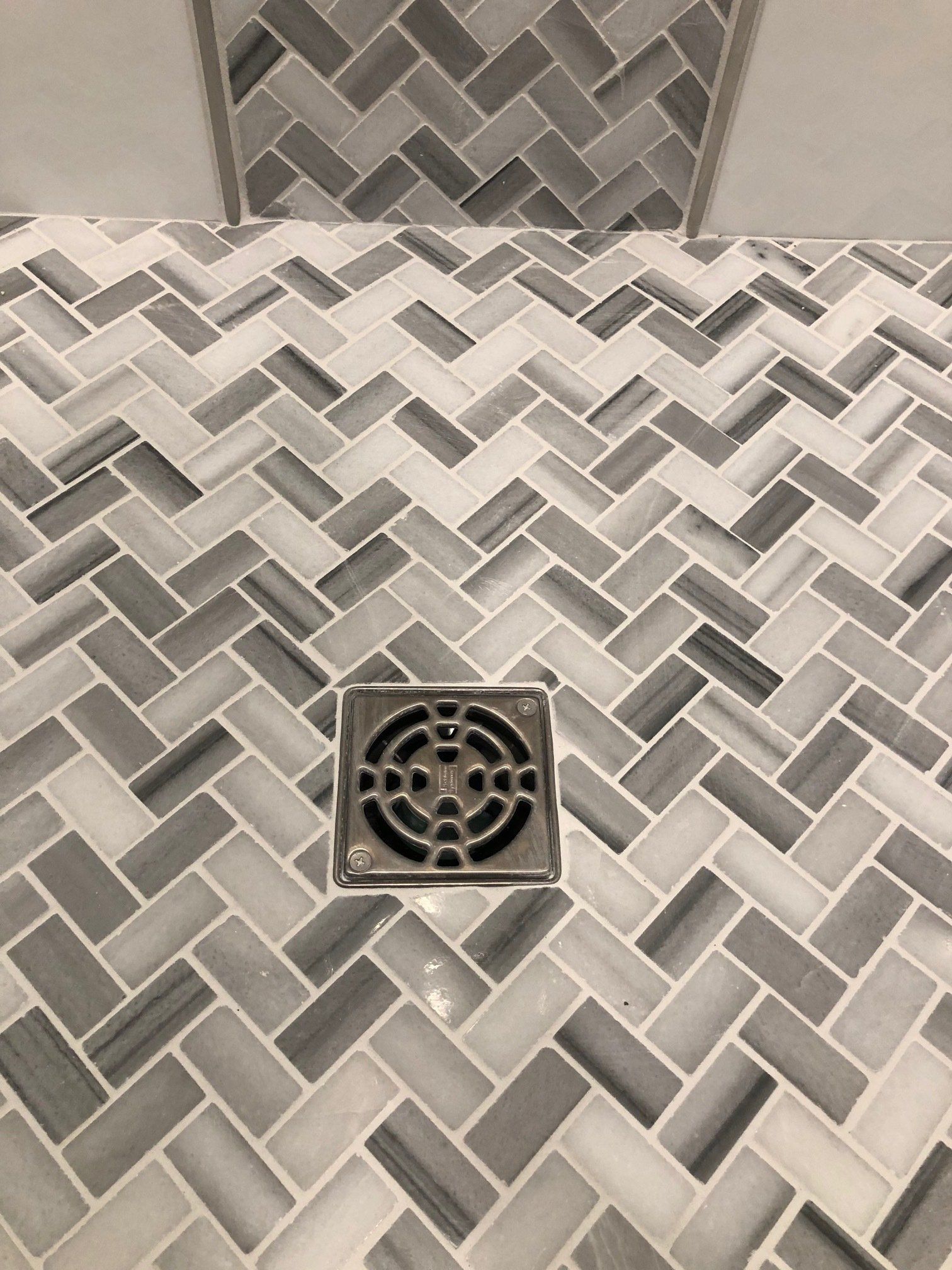 A shower floor with a herringbone pattern and a drain.