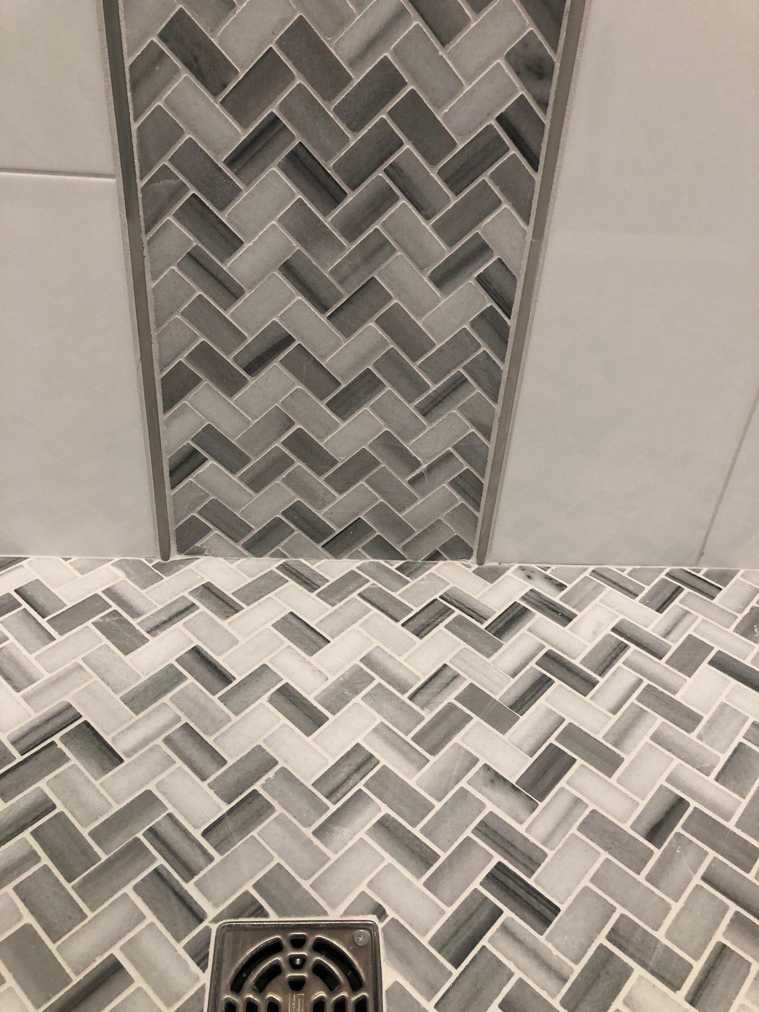 A close up of a shower floor with a herringbone pattern and a drain.