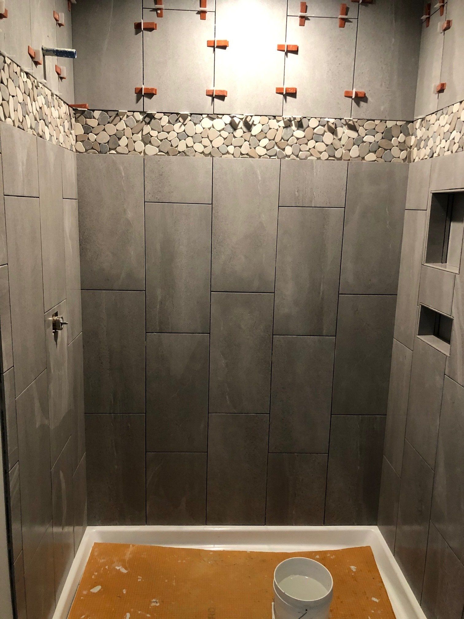 A shower stall with tiles being installed and a bucket of paint on the floor.