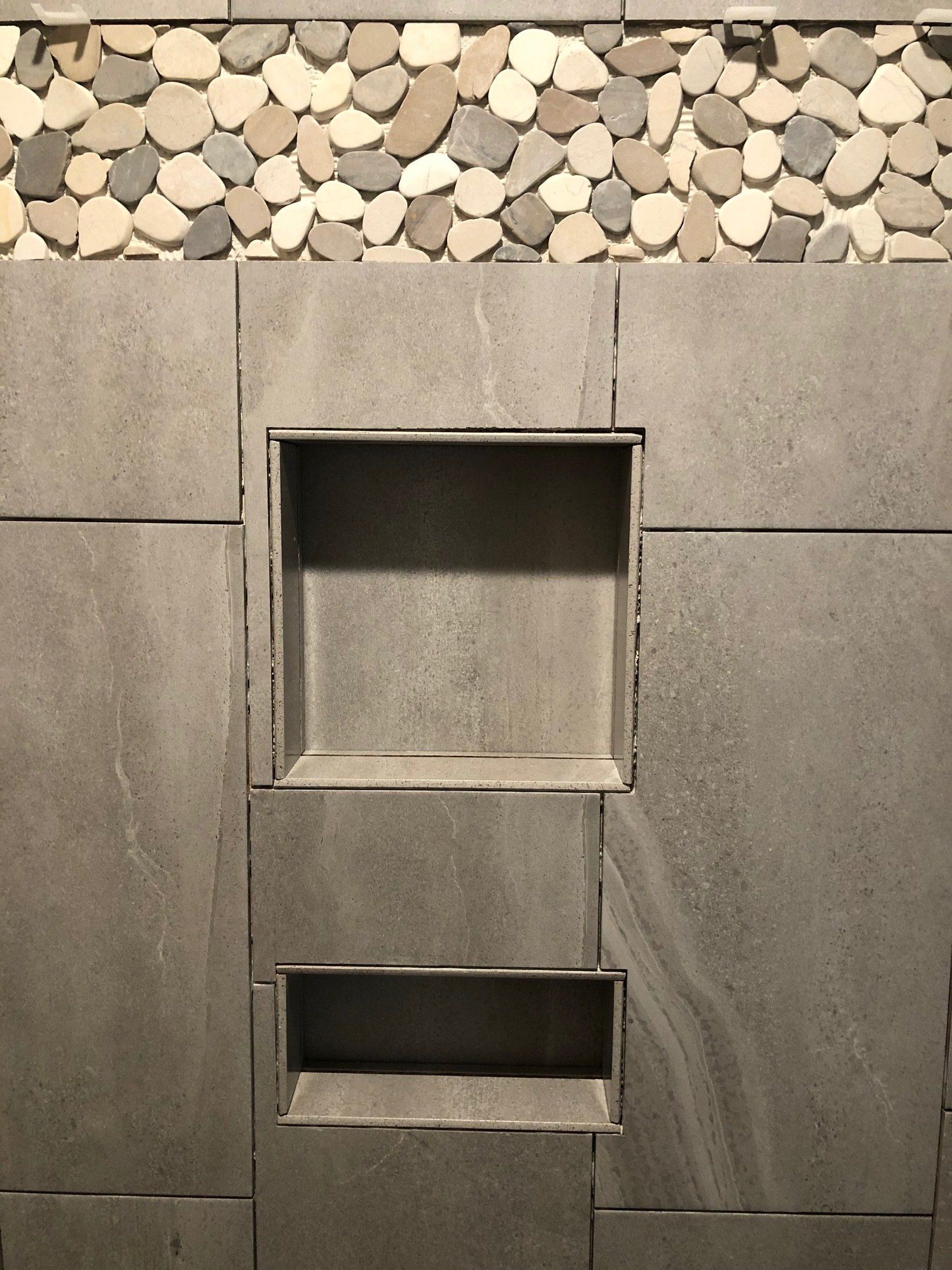 A tiled wall with two shelves and a stone border