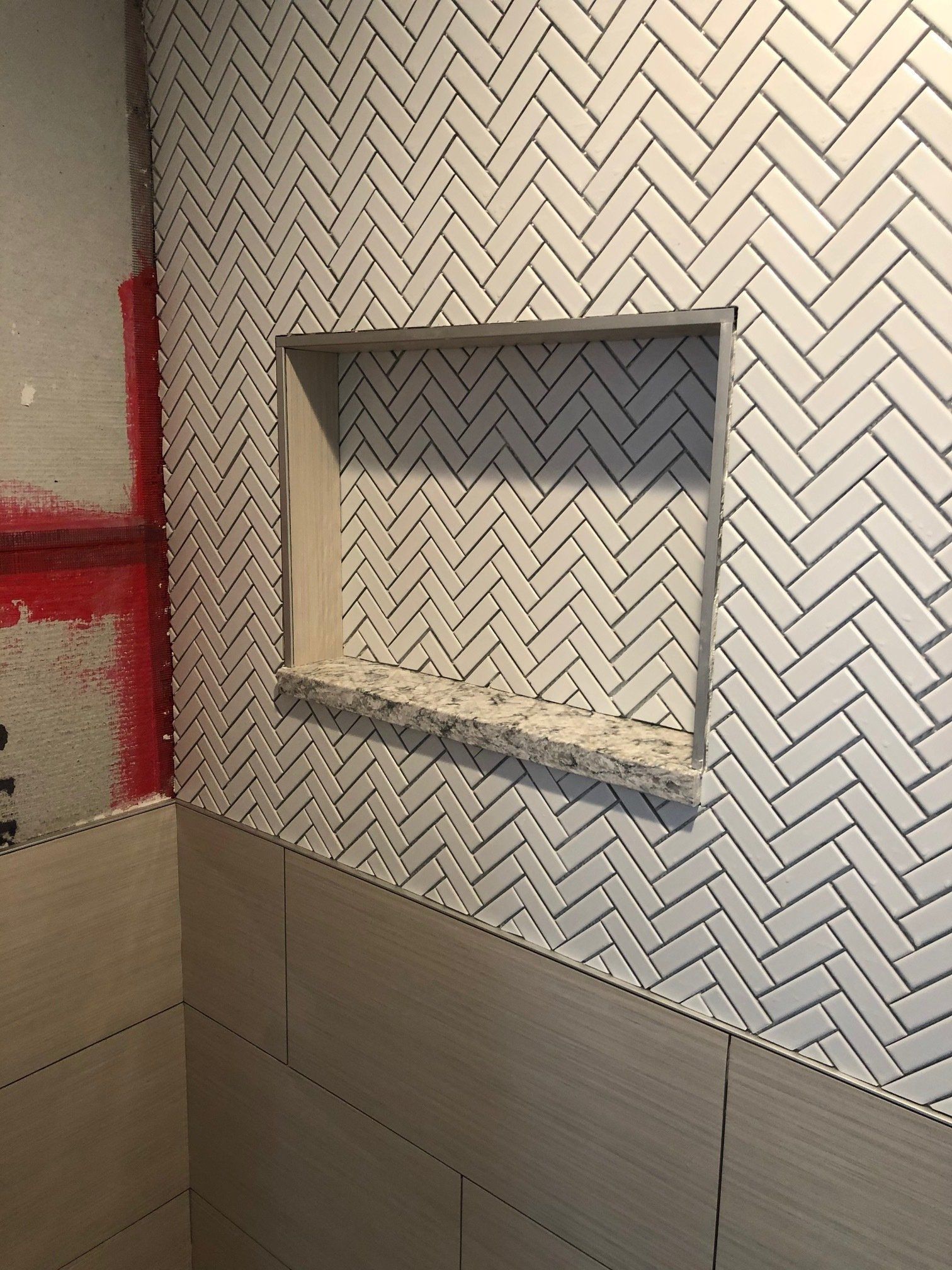 A shower niche in a bathroom with a herringbone pattern on the wall.