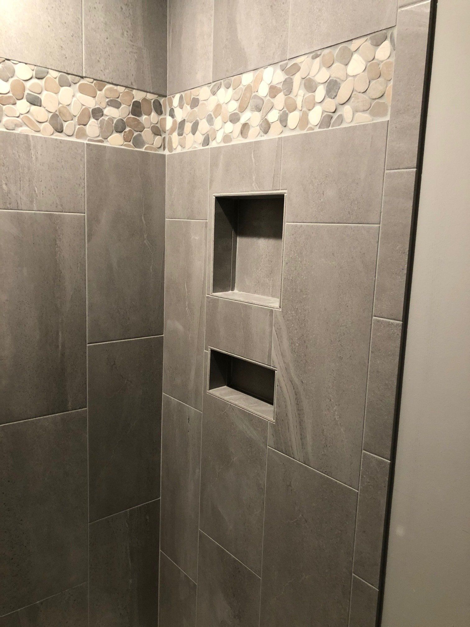 A shower with two shelves and a stone border on the wall.