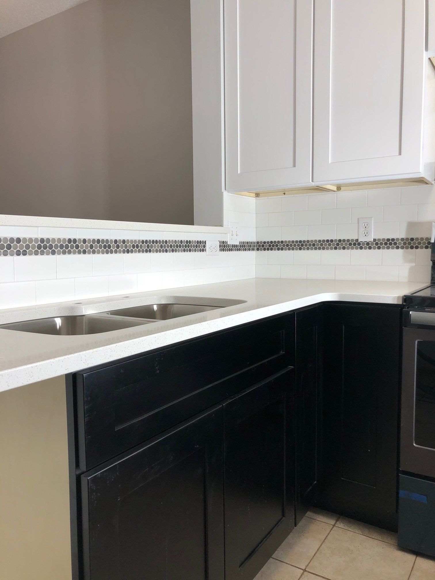 A kitchen with black cabinets , white counter tops , a sink and a stove.