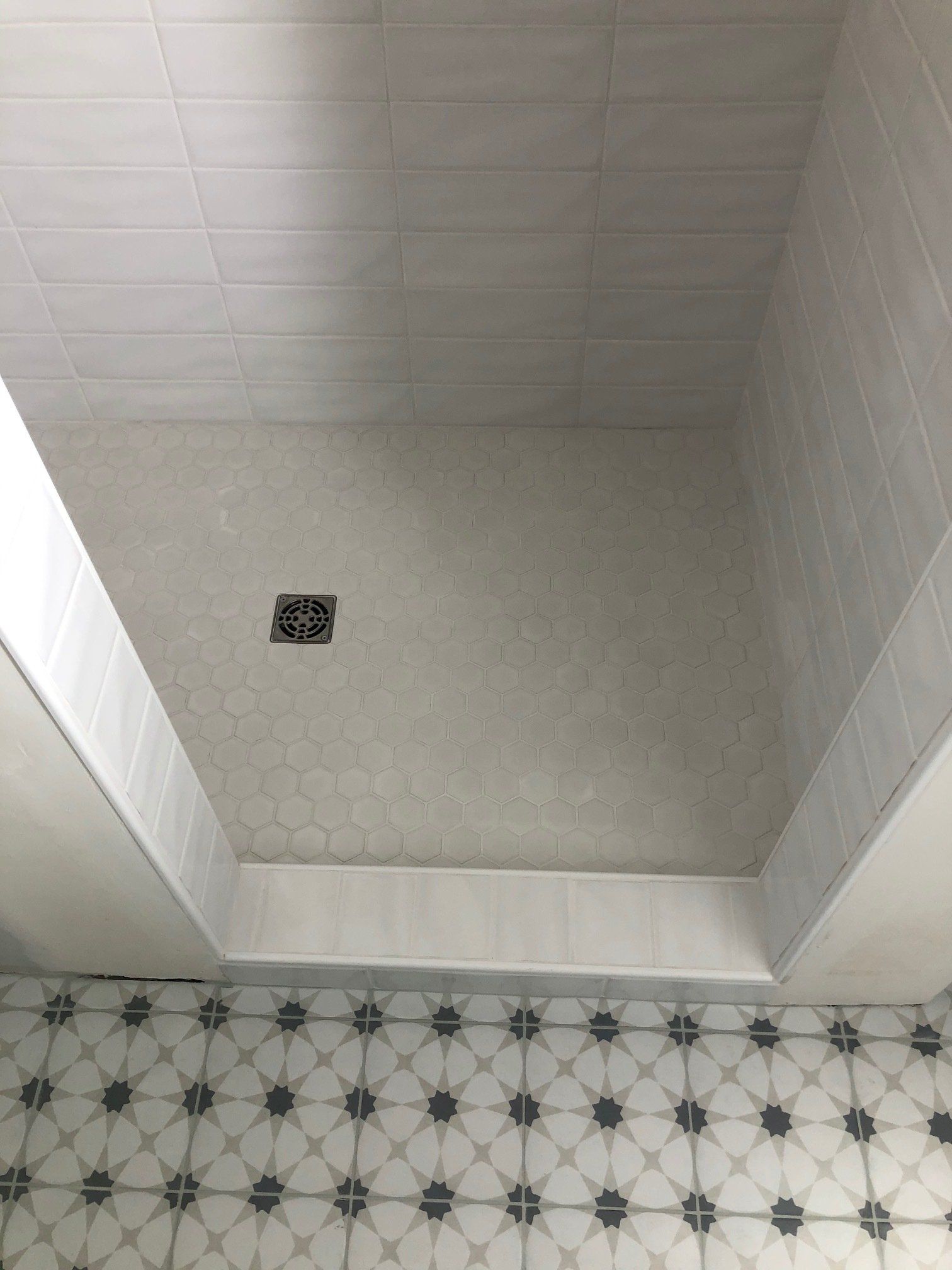 A shower stall with white tiles and black and white tiles on the floor.