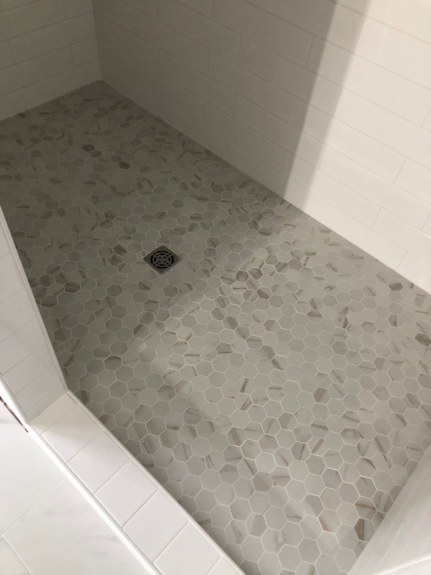 A walk in shower with white tiles and a drain.