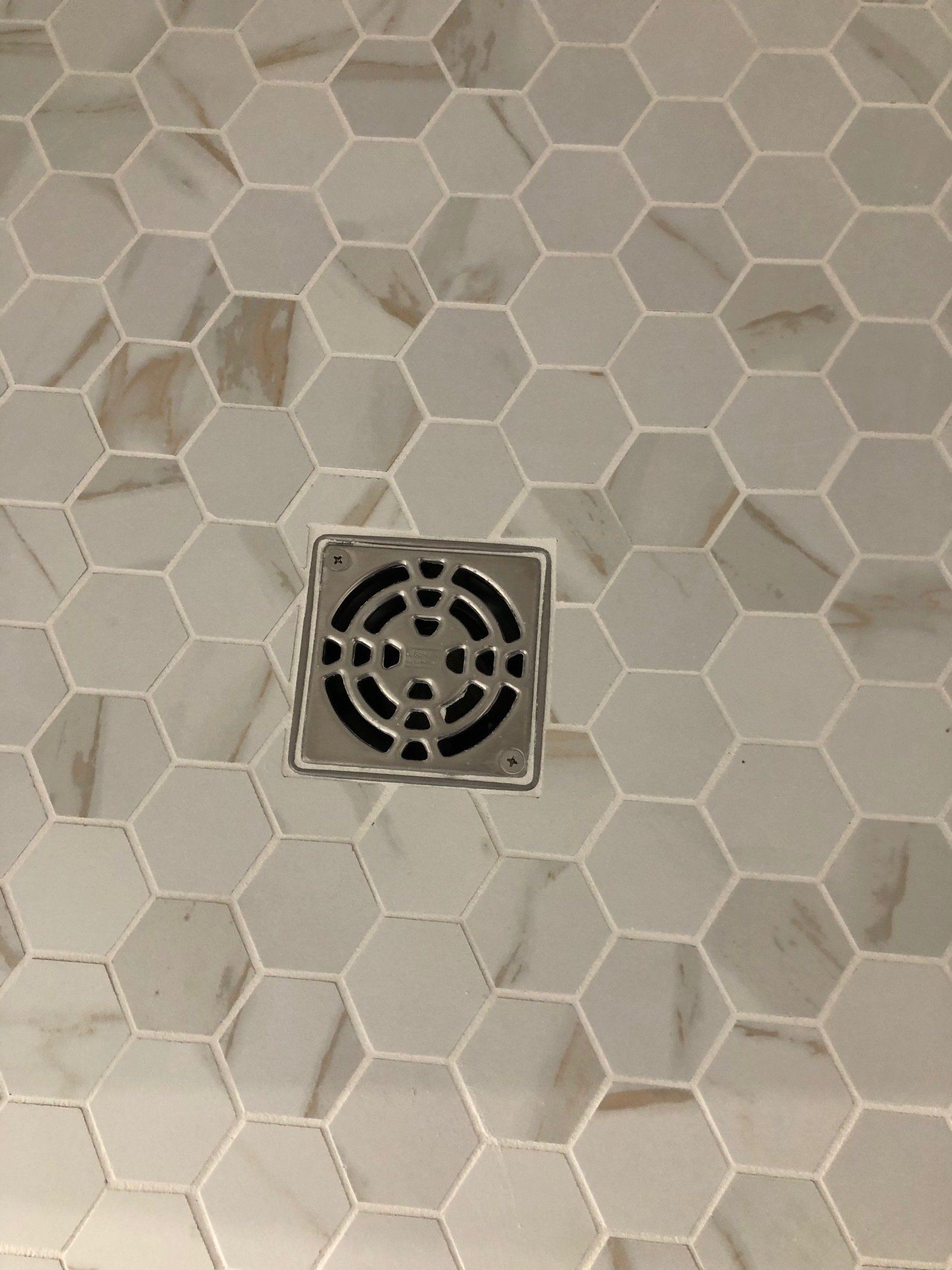 A shower floor with hexagonal tiles and a drain.