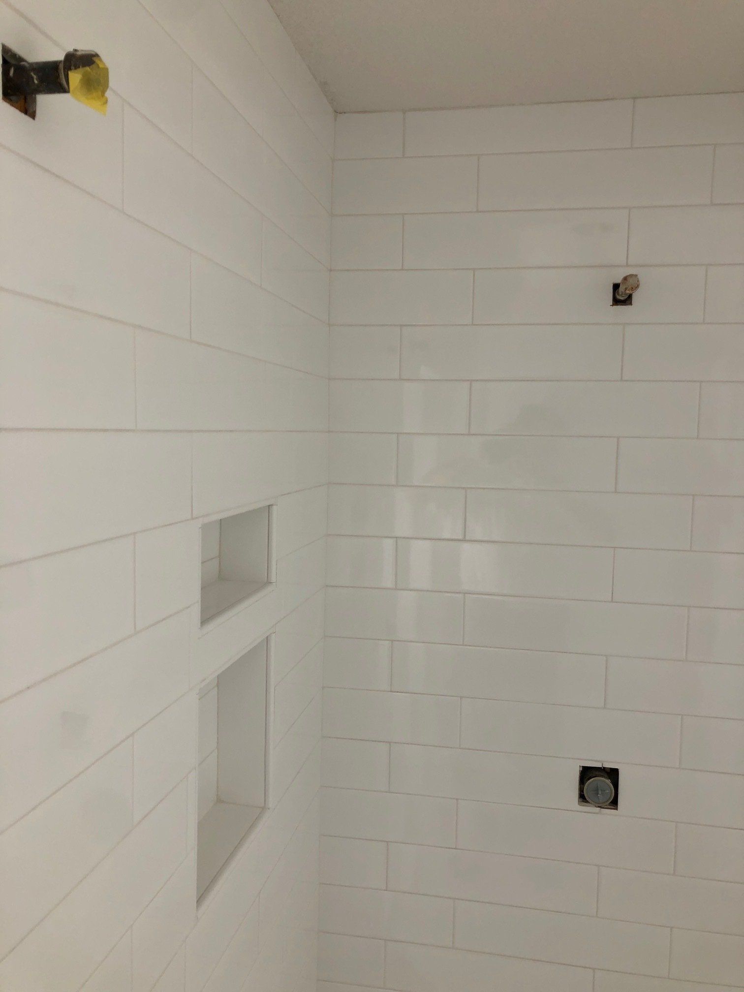 A bathroom with white tiles and a shower head.