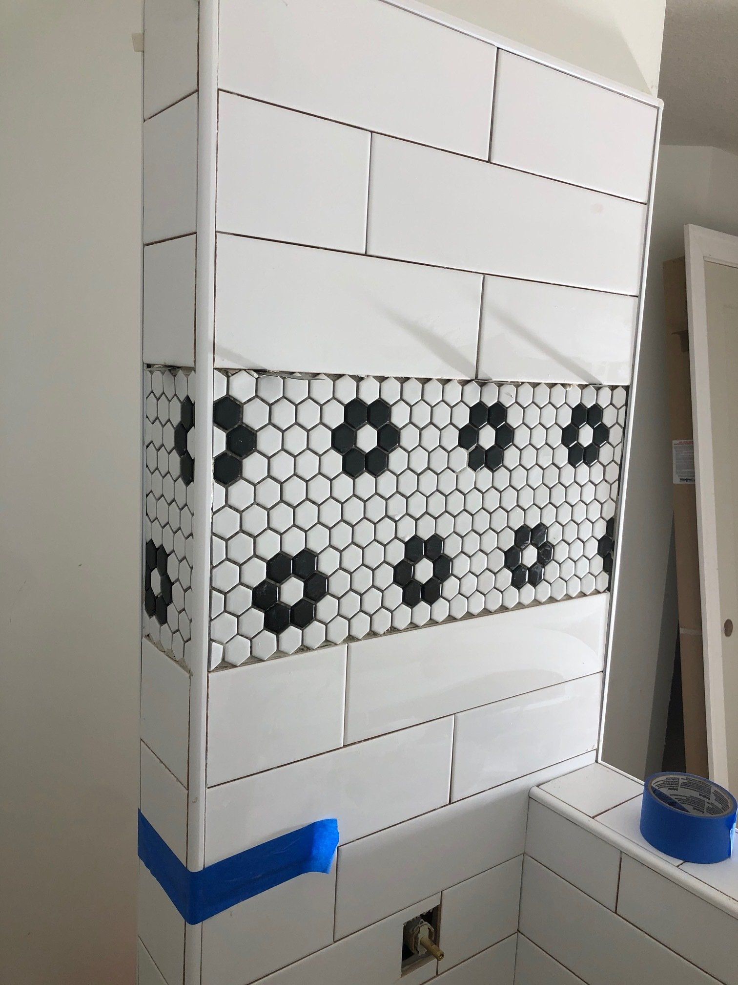 A bathroom wall with white tiles and black flowers on it.
