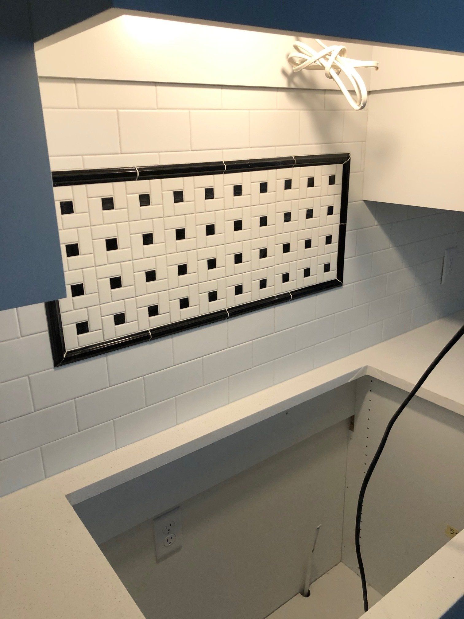 A kitchen with white tiles and black squares on the wall.