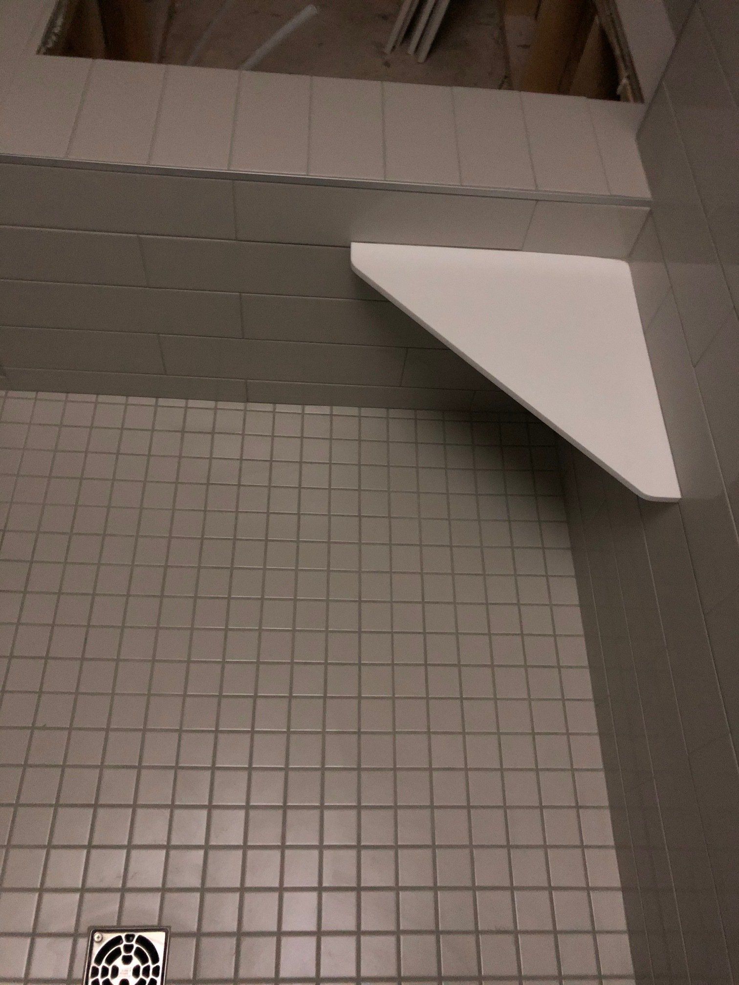 A bathroom with a drain and a corner shelf