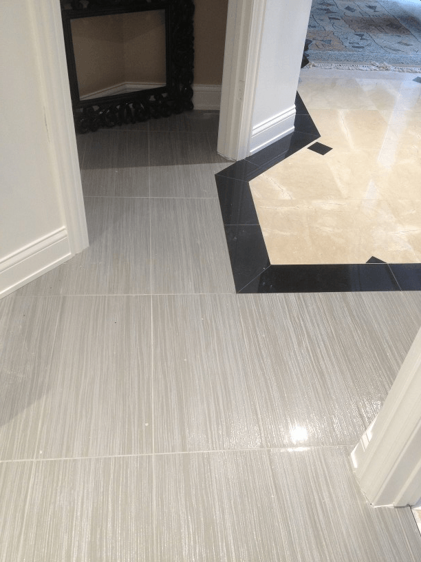A tiled floor with a black border and a fireplace in the background
