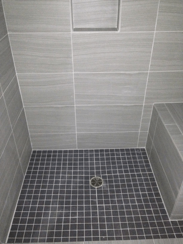 Renovated shower stall with a black tile floor and a drain.