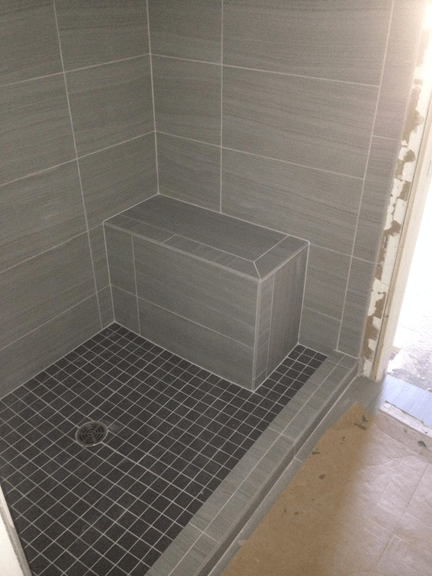 A handicap shower stall with a bench in the corner.